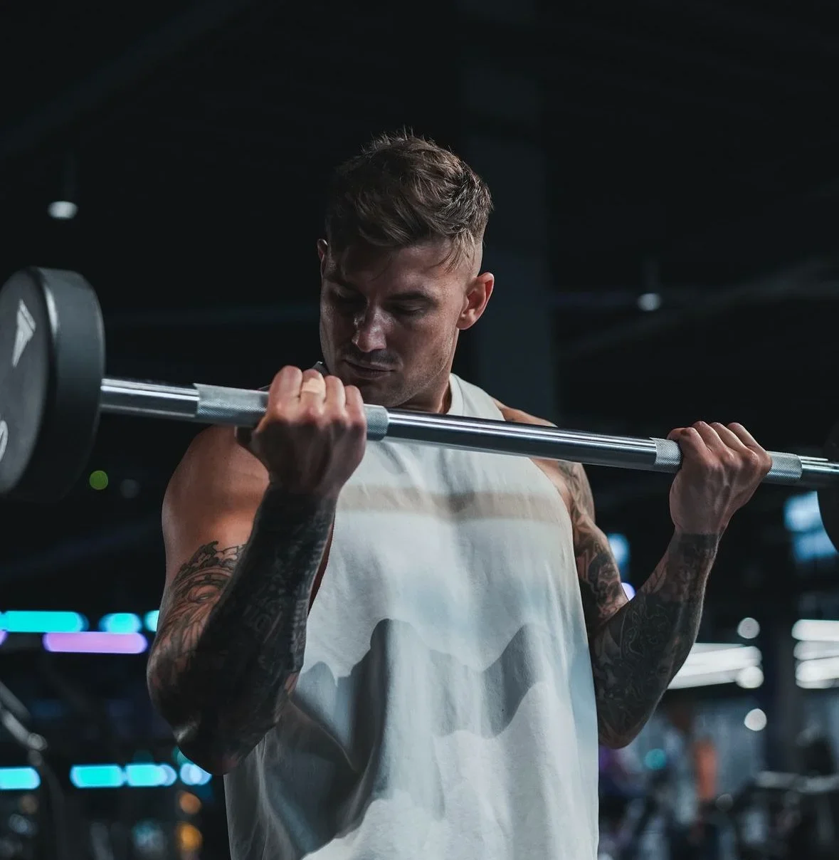 A young man lifts a barbell with weights in a gym, focusing on his workout.