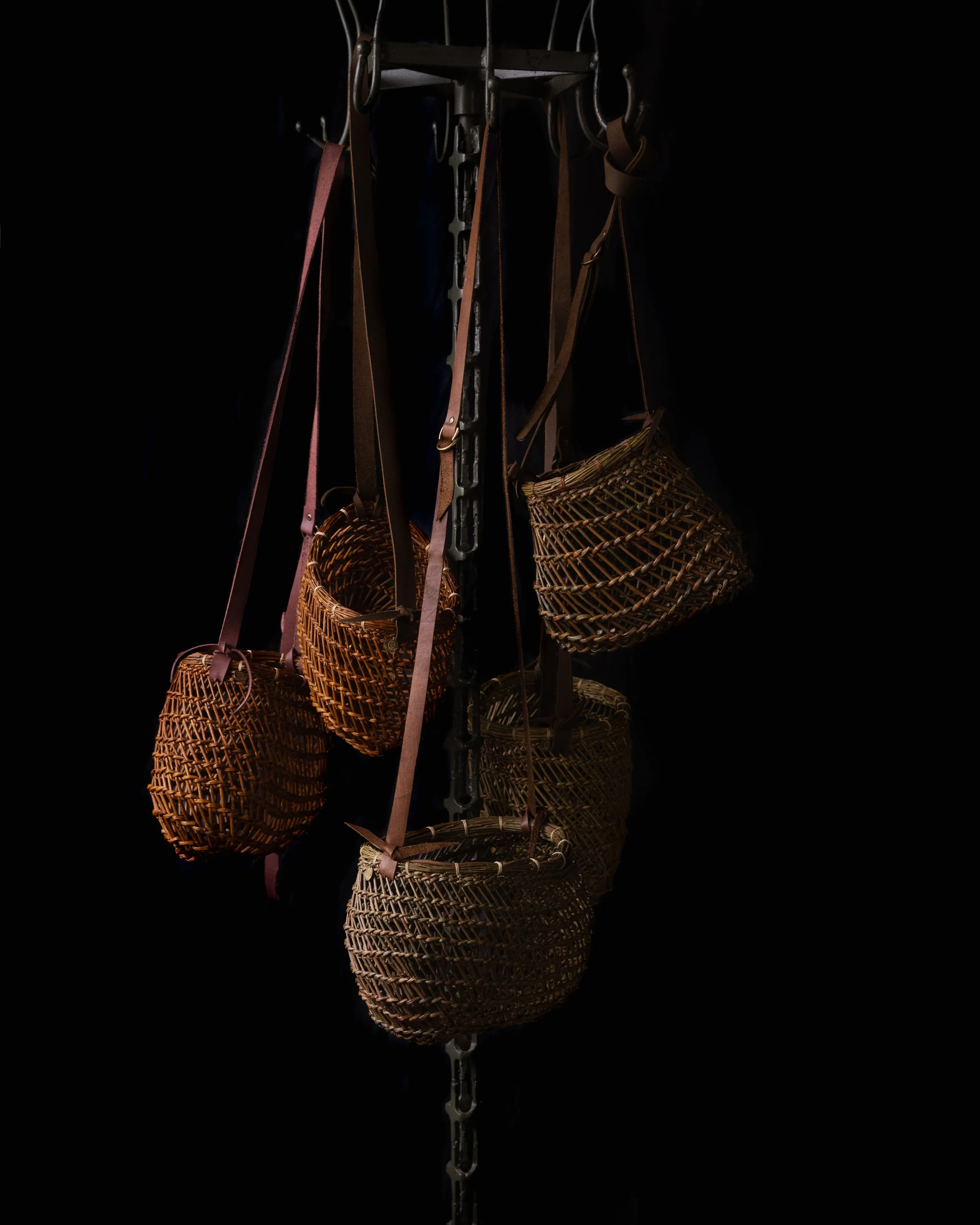 Multiple woven baskets hanging from hooks on a metal stand, with a dark background.