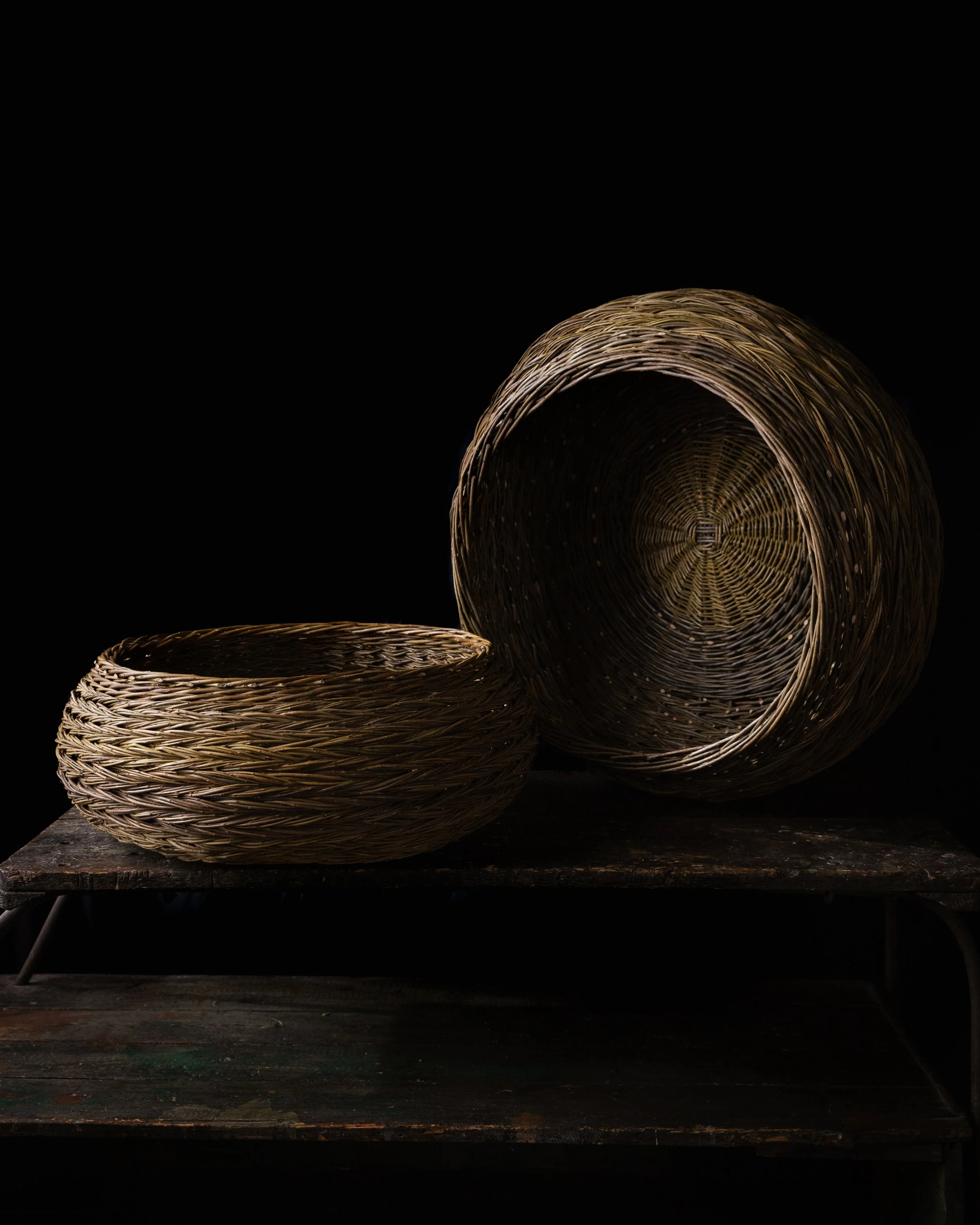 Two woven baskets, one large and one small, are placed on a dark wooden surface against a black background.