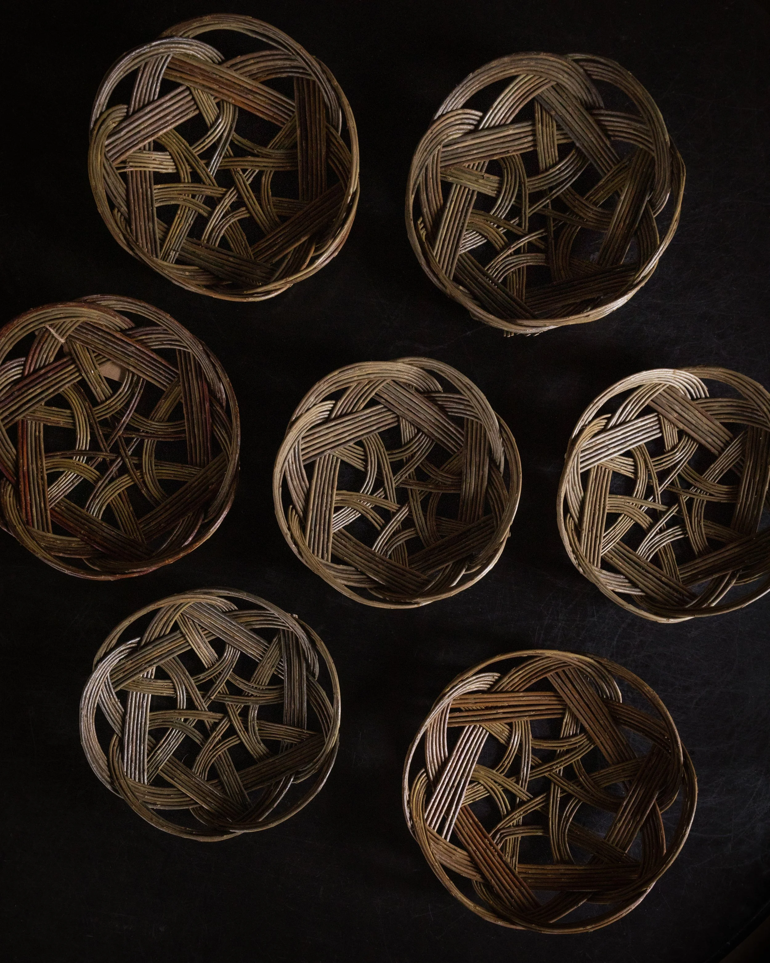 Nine small woven baskets arranged on a dark surface.