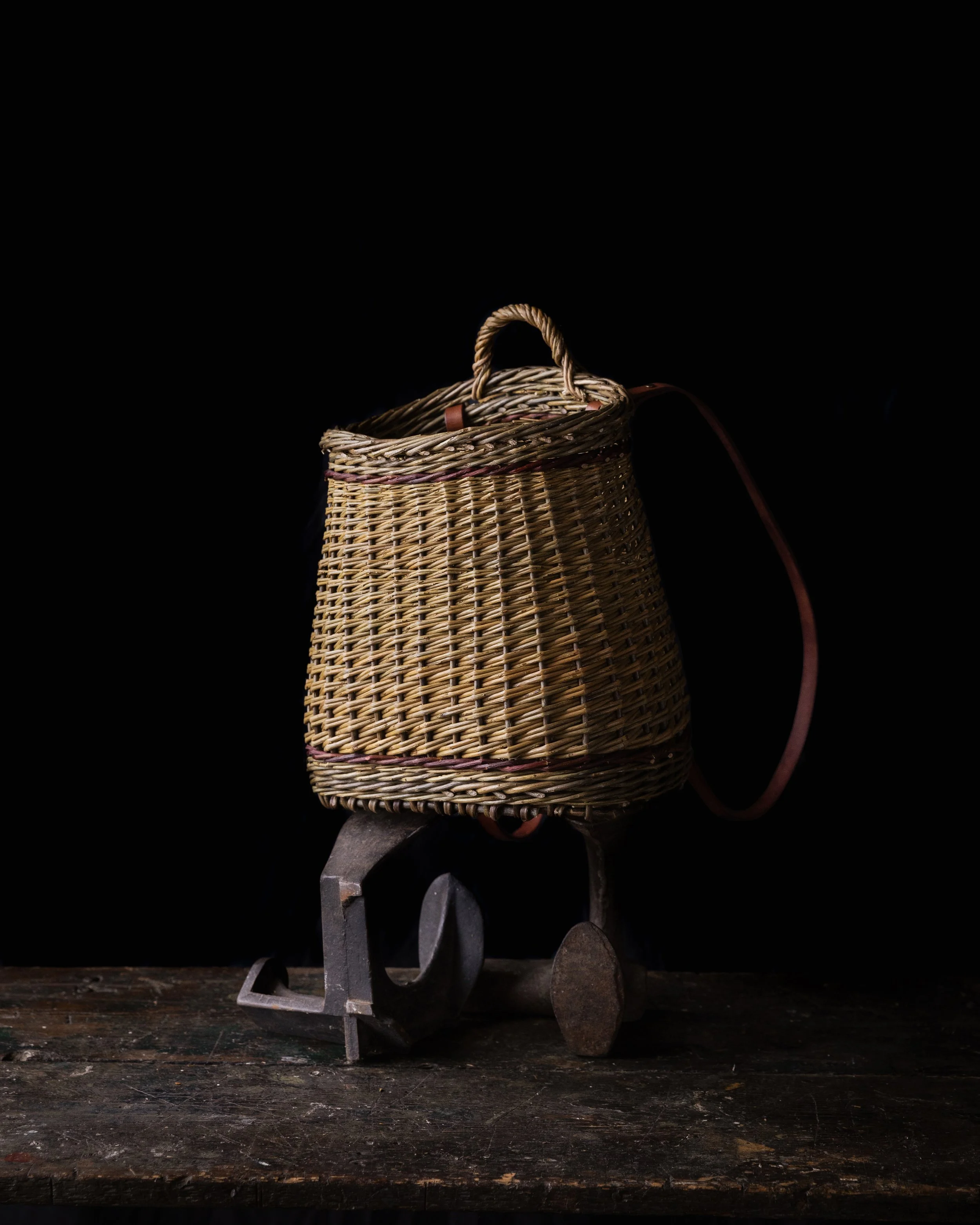 Wicker bag with leather strap on a vintage metal toy vehicle, placed on a wooden surface, dark background