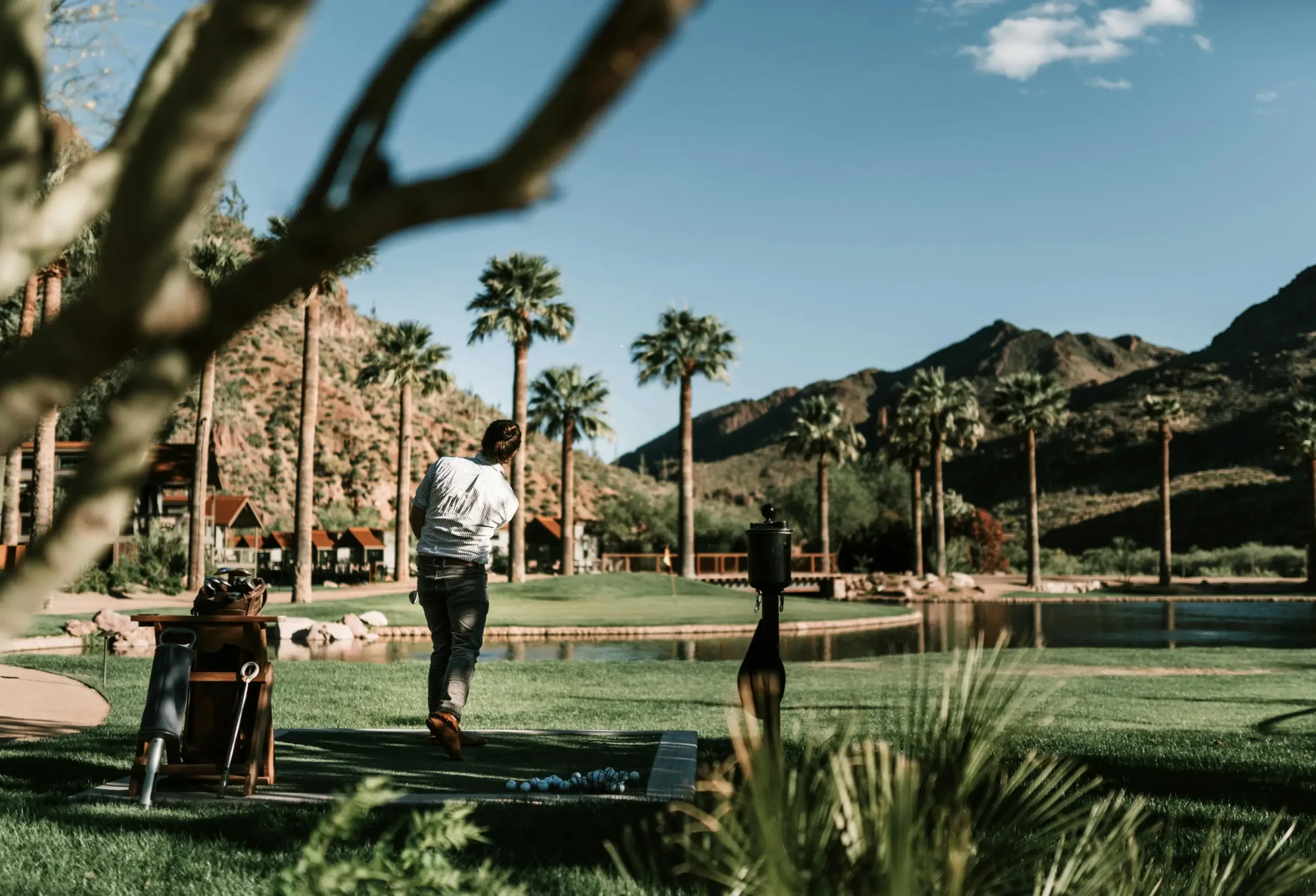 A person playing mini golf on a course with mountains and palm trees in the background.