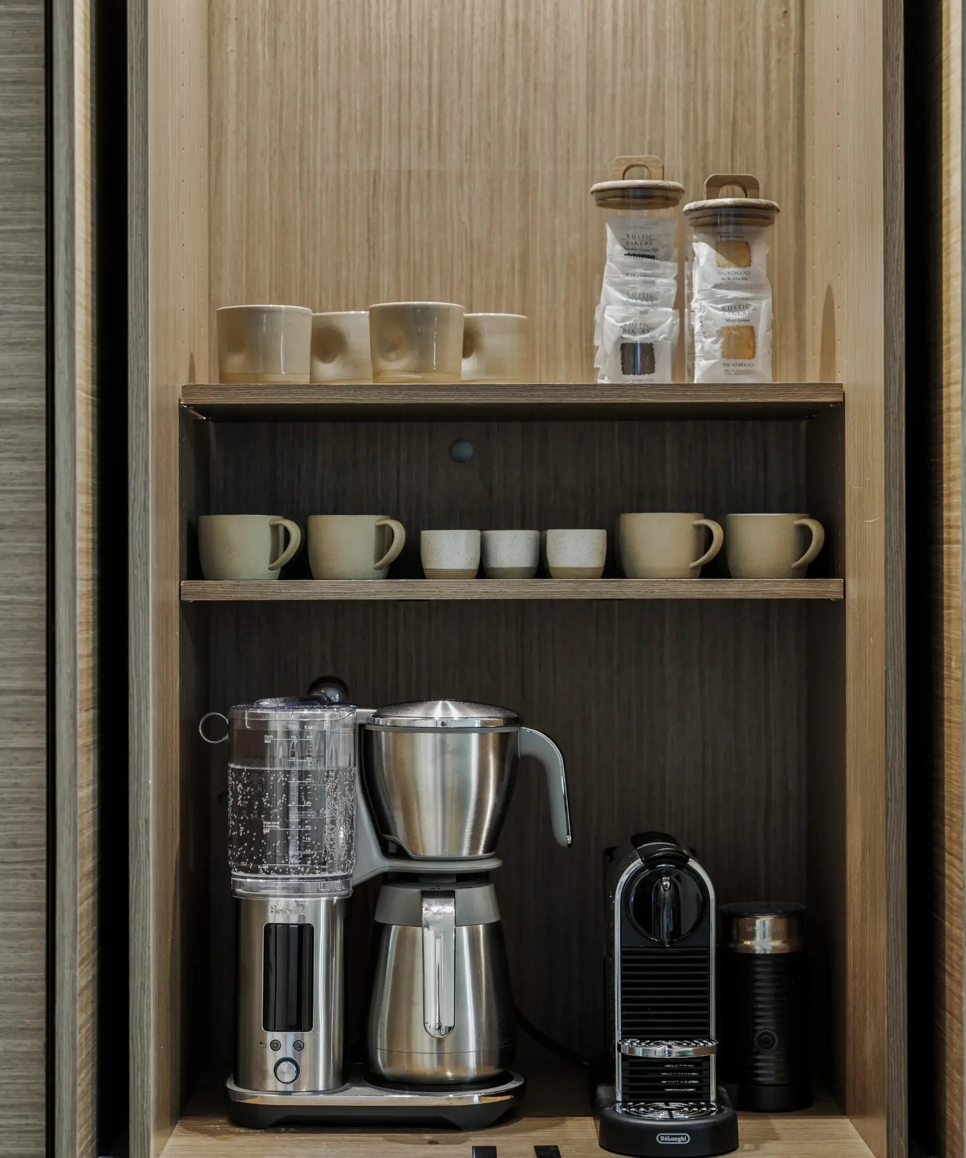 Kitchen cabinet with coffee cups, jars of coffee beans, coffee maker, blender, and espresso machine.
