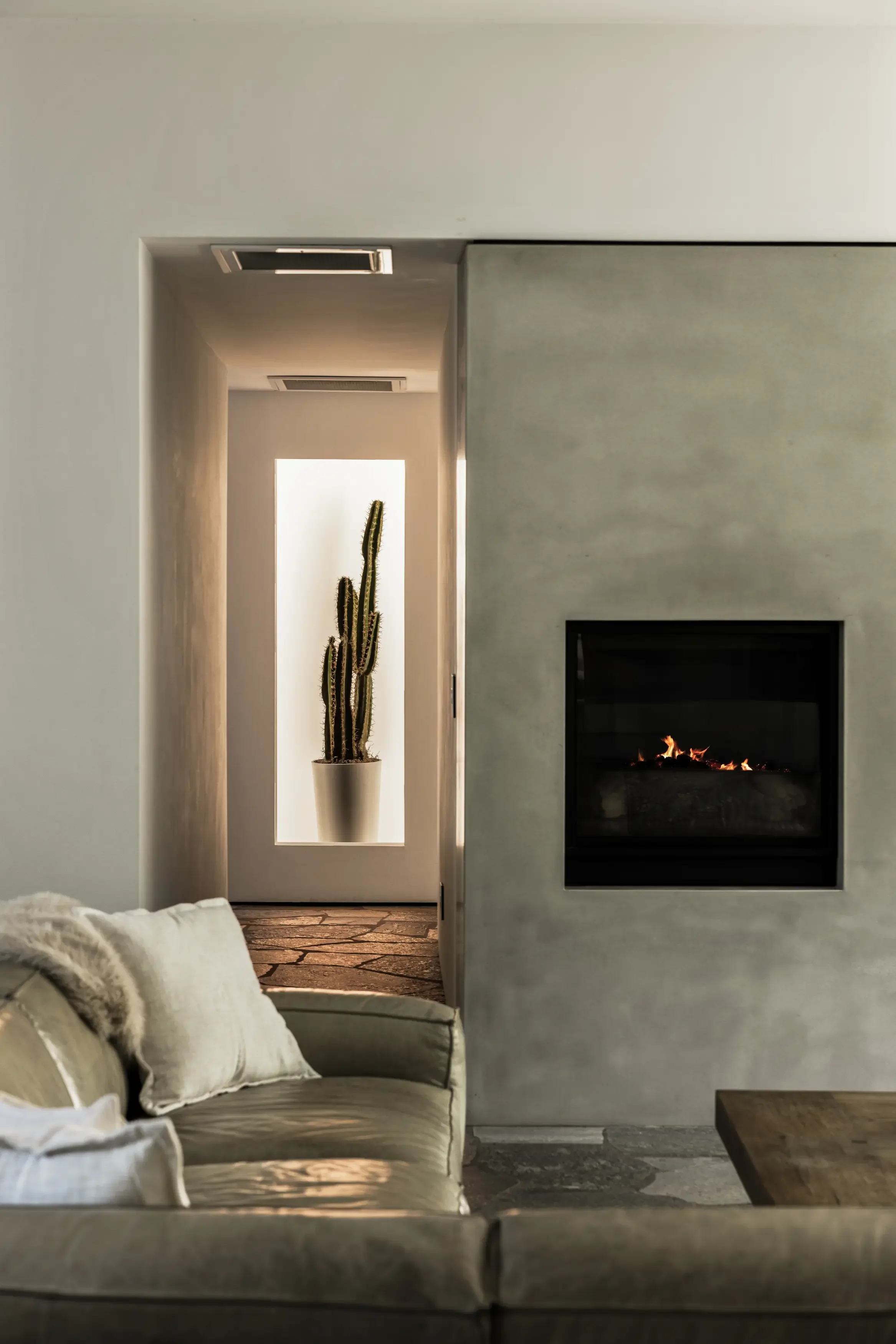 Modern living room with a beige couch, a fireplace, and a hidden cactus in a vertical niche with frosted glass.