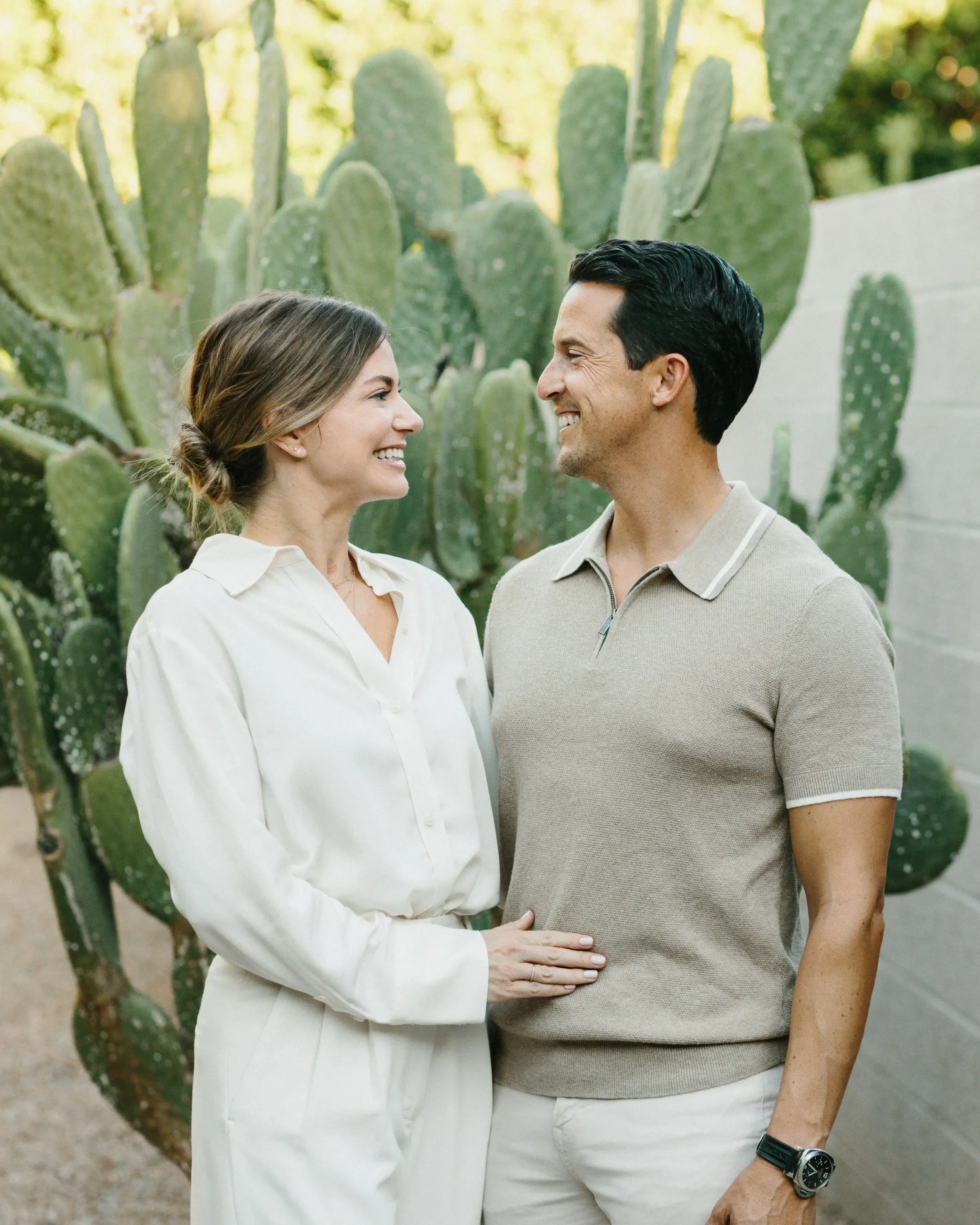 A smiling woman and man looking at each other in front of large cactus plants.