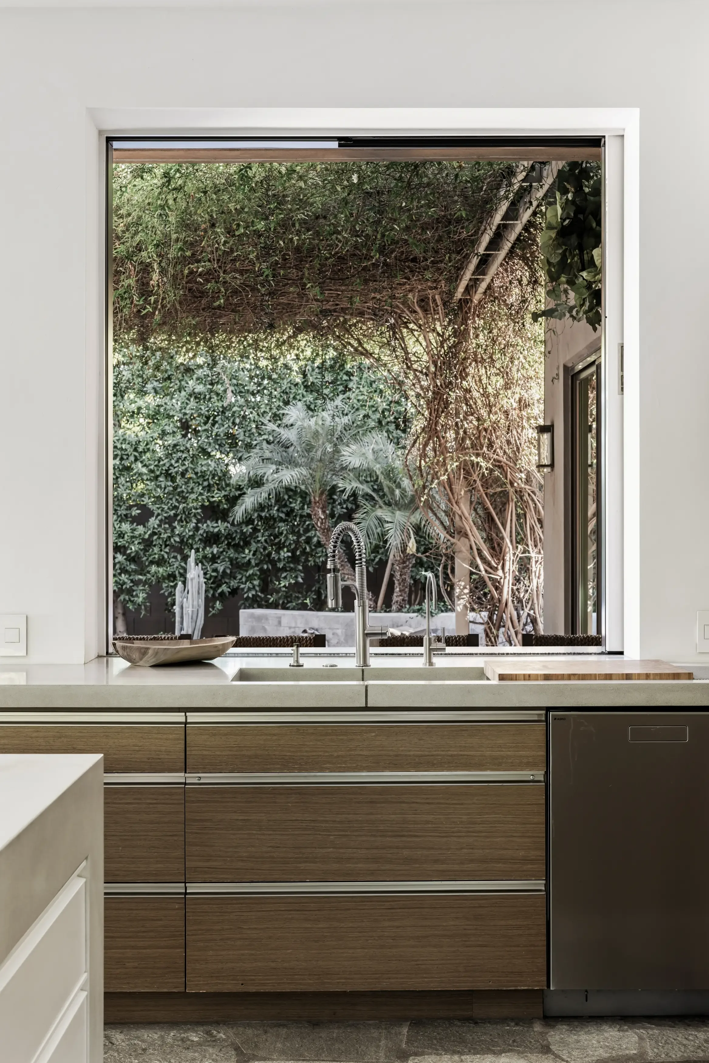 Modern kitchen with a large window overlooking lush vegetation and trees outside.