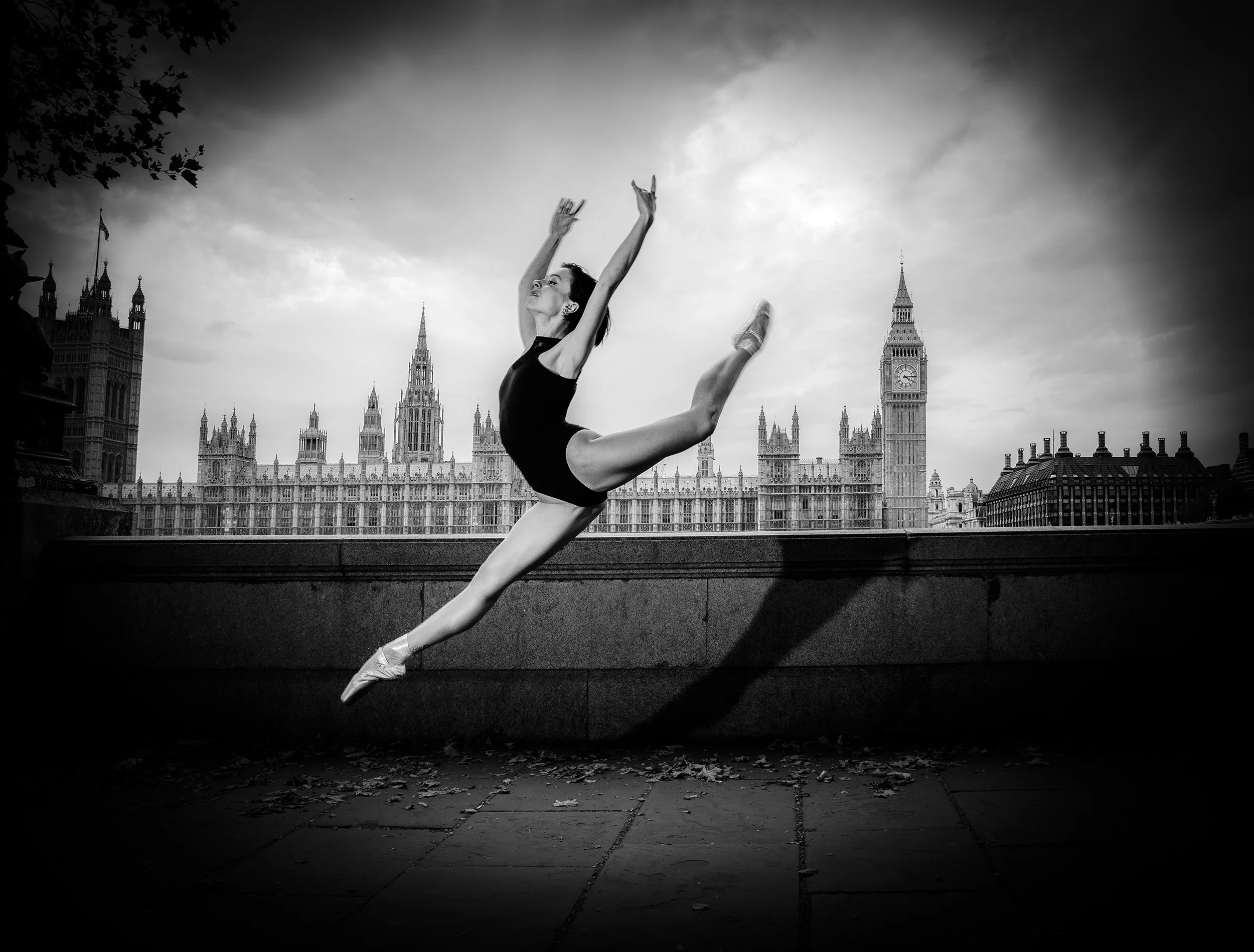 A ballet dancer performing a leap near Westminster London landmarks, including Big Ben, in the background, black and white photo.