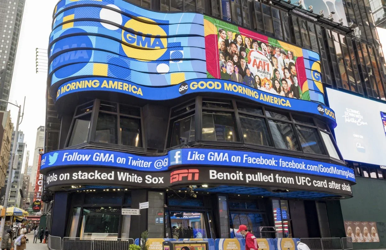 Billboards on a city building advertising ABC's Good Morning America, ESPN, and social media pages, with a digital display showing a collage of women and the words 'Women March AAPI'.