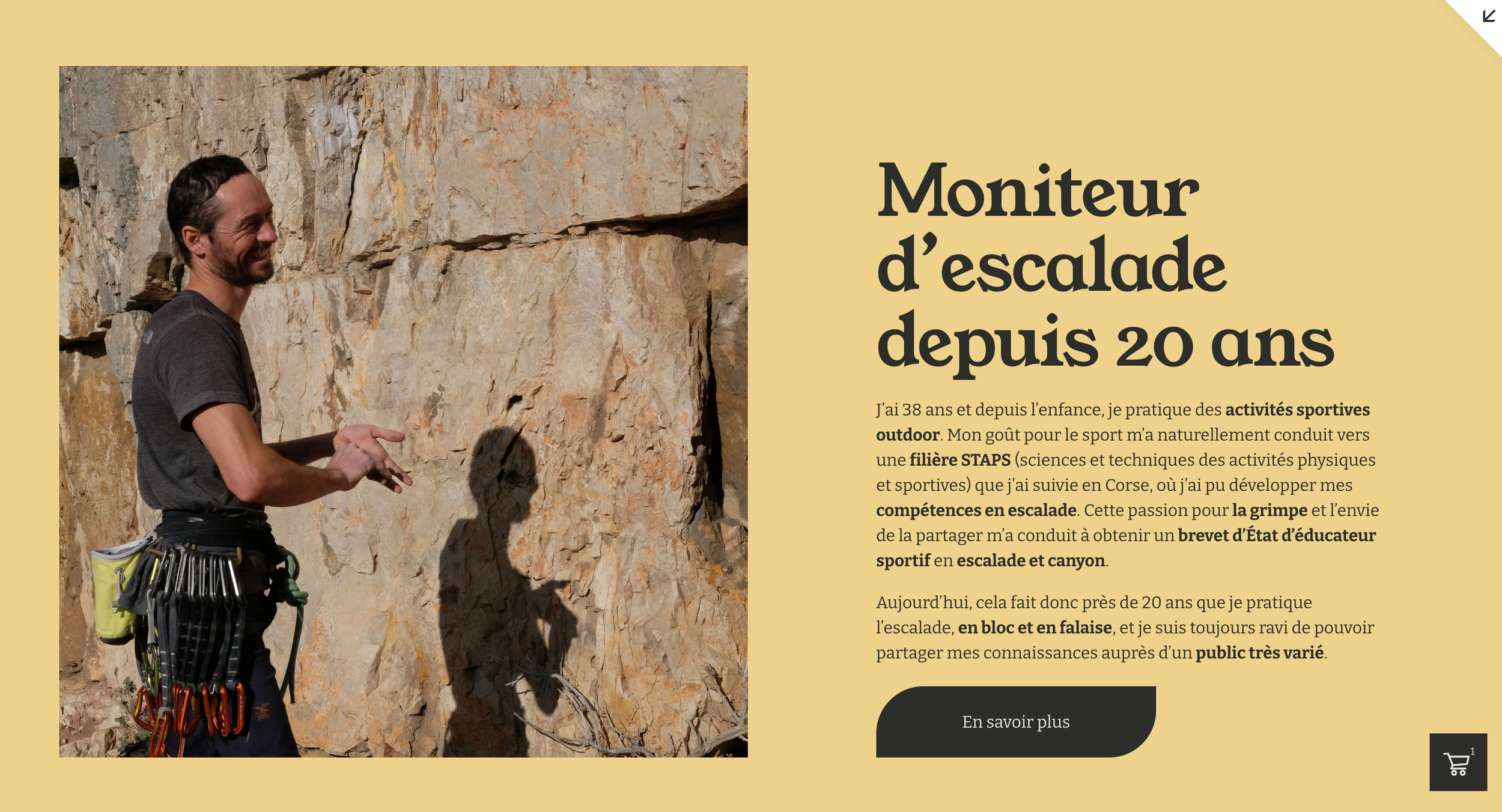 Un homme portant un pantalon noir et un t-shirt gris, équipé de nombreux mousquetons accrochés à la ceinture, sourit face à un mur d'escalade en roche naturelle.