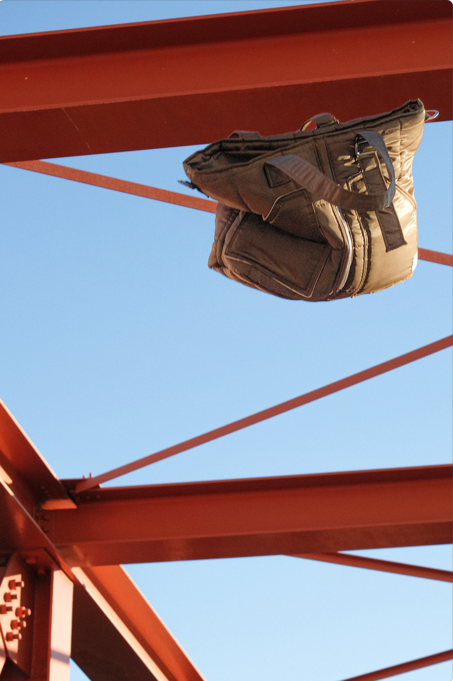 Un sac à dos suspendu sous une structure rouge en métal contre un ciel bleu.