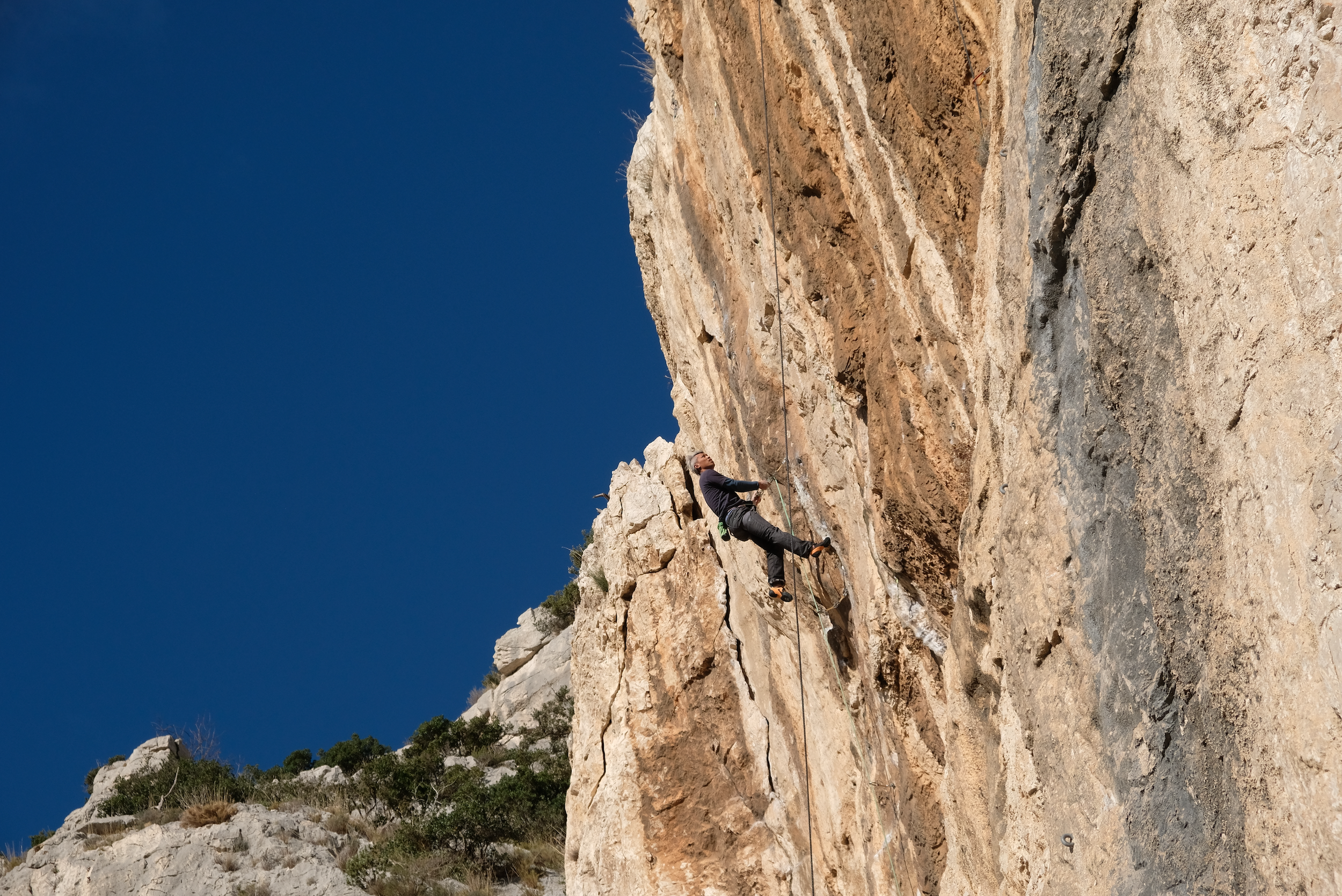Personne en train d'escalader une falaise rocheuse sous un ciel bleu.