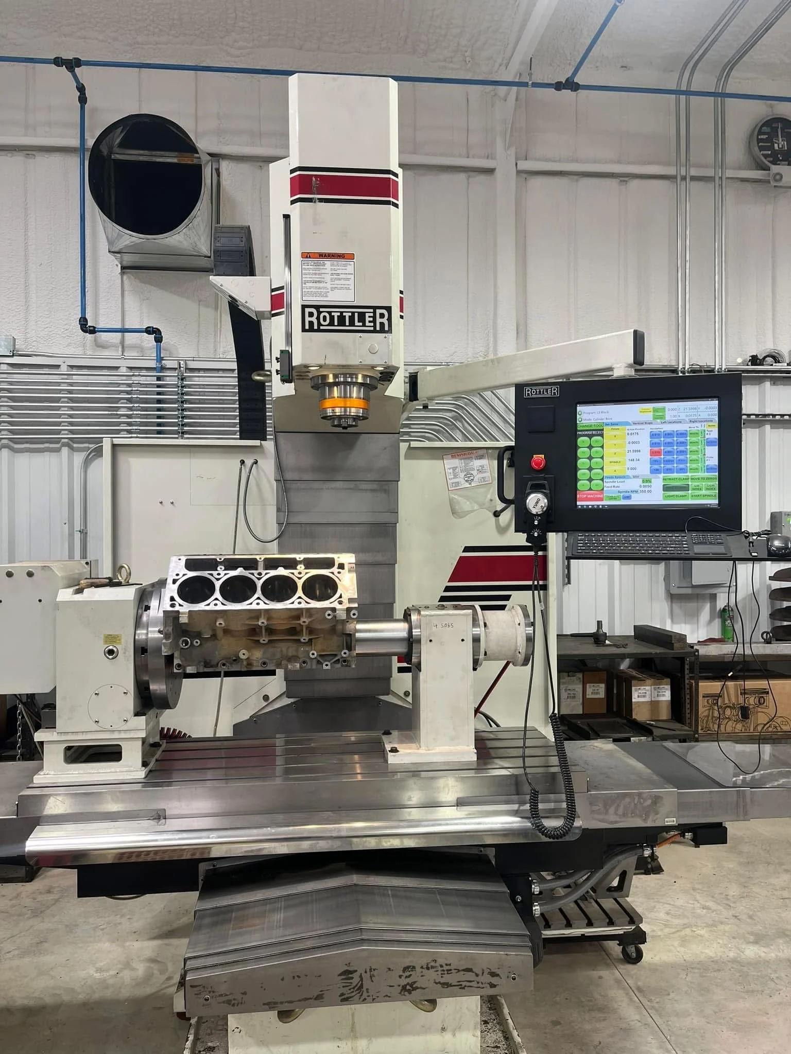 A CNC milling machine cutting a block of metal in an industrial workshop. The machine has a computer interface on the right for control.