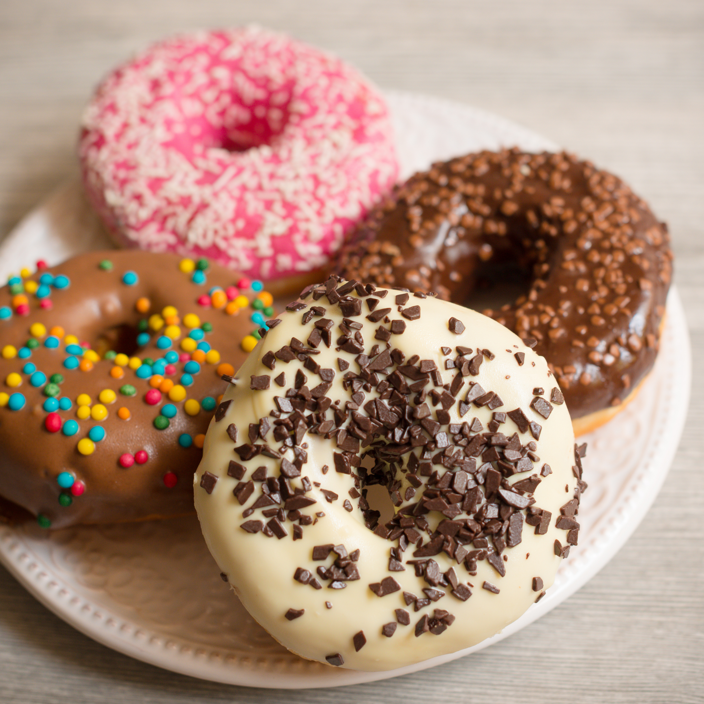 Four decorated donuts on a white plate, with pink, brown, and white icing and colorful sprinkles.