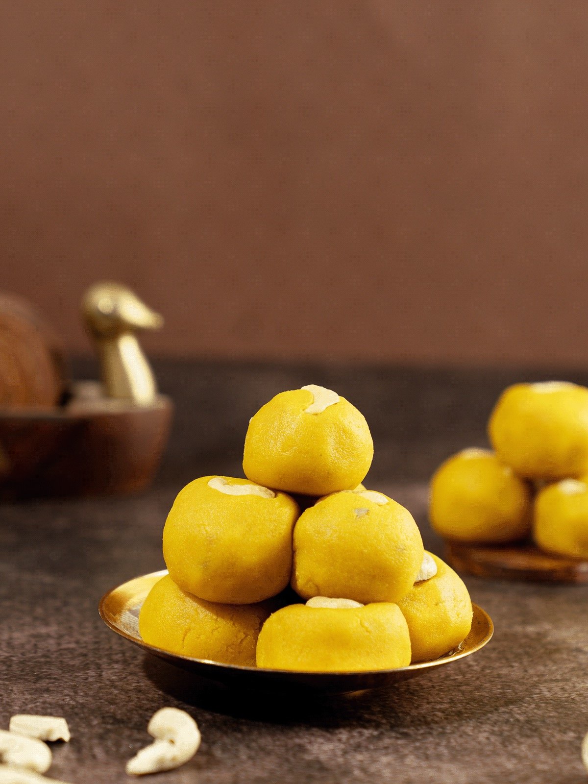 A small gold-colored bowl filled with yellow sweets stacked in a pyramid on a dark surface.