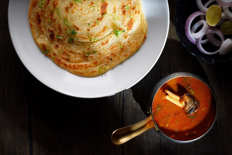 Indian meal with a plate of naan bread, a bowl of onion rings, and a pot of spicy fish curry.