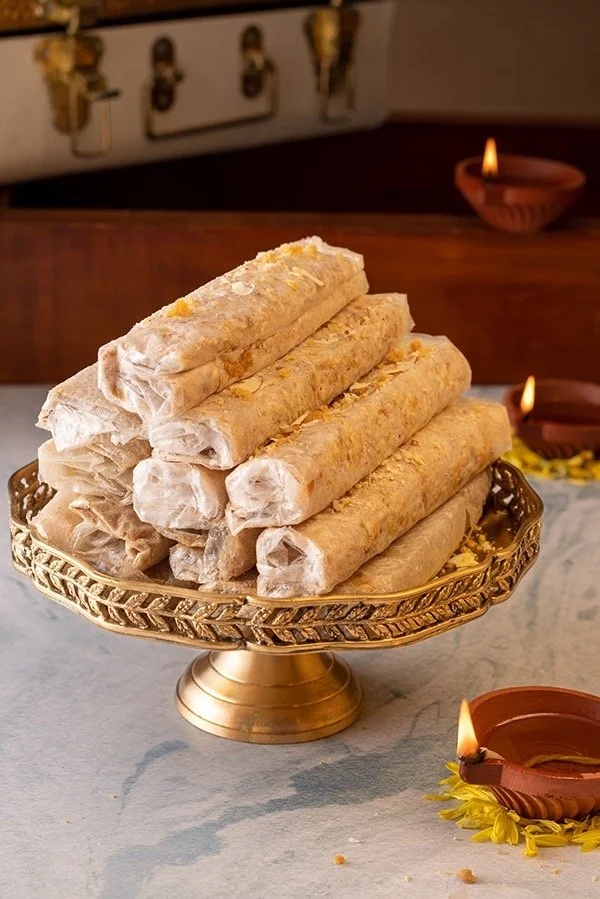 Stack of five traditional Indian snacks called samosas on a golden ornate tray, with oil lamps in the background, decorated for a festive occasion.
