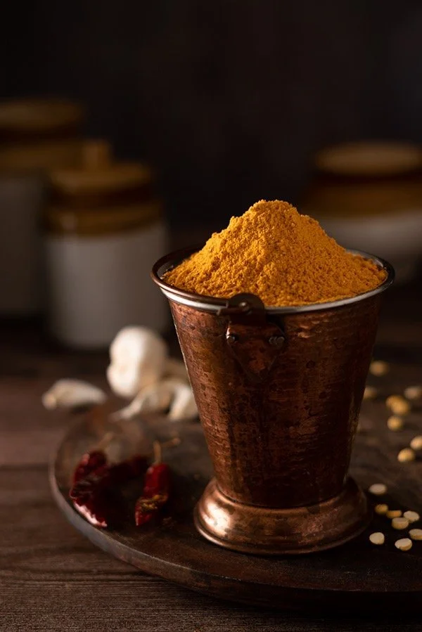 A copper cup filled with bright yellow turmeric powder on a dark wooden surface.