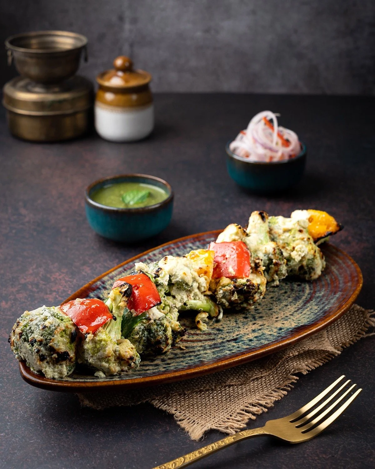 Vegetable roll appetizer with red pepper, served on a ceramic plate, with dipping sauces and condiments in small bowls on a dark table.