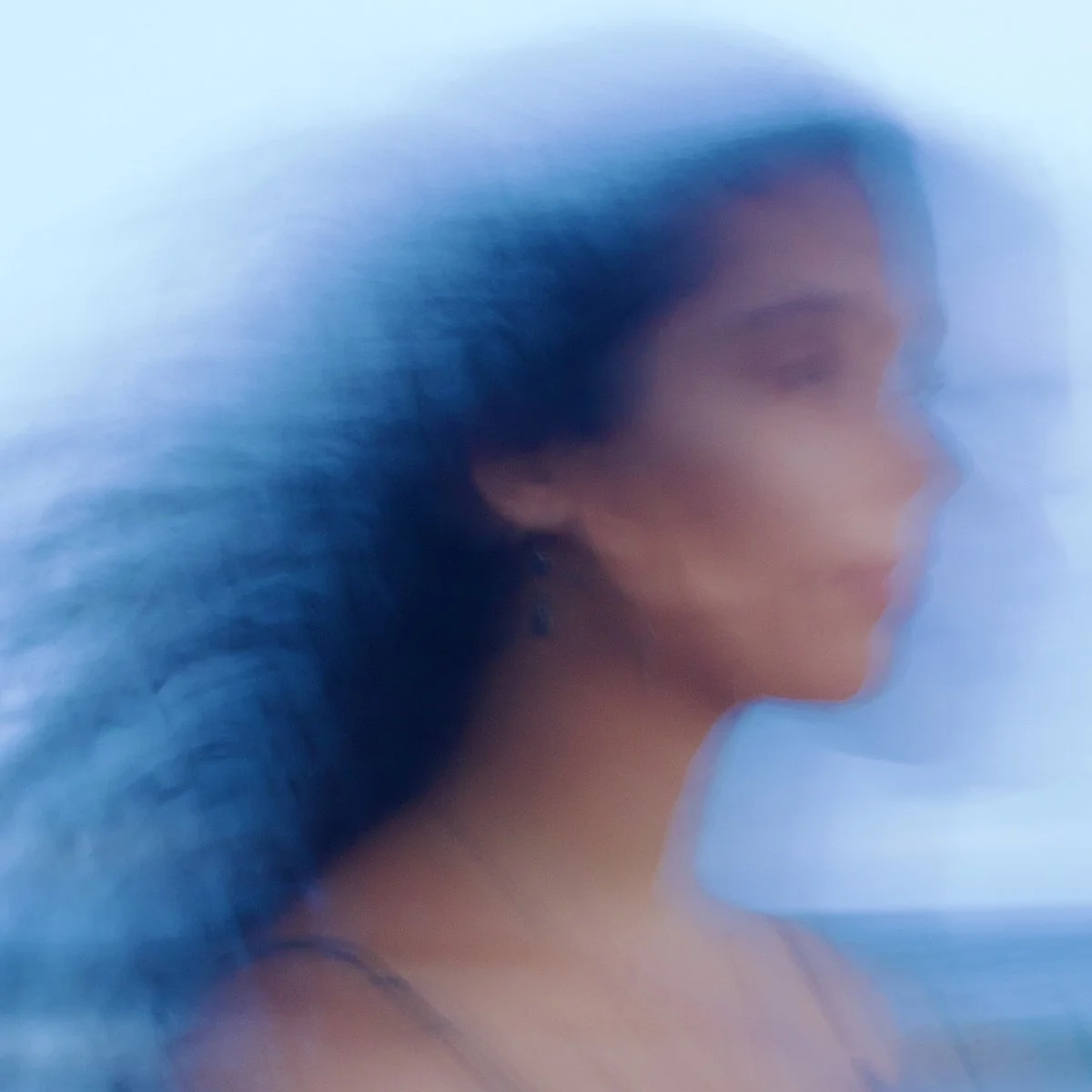 A blurred profile of a woman's face and hair against a light blue background.