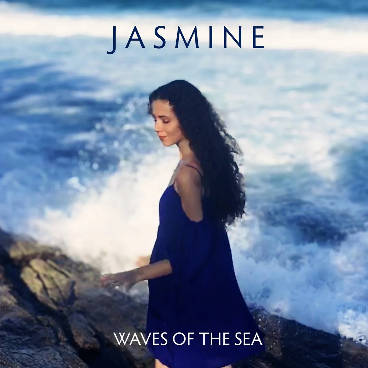 A woman with long dark curly hair standing on rocks at the beach as waves splash around her, with the word 'Jasmine' at the top and 'Waves of the Sea' at the bottom.
