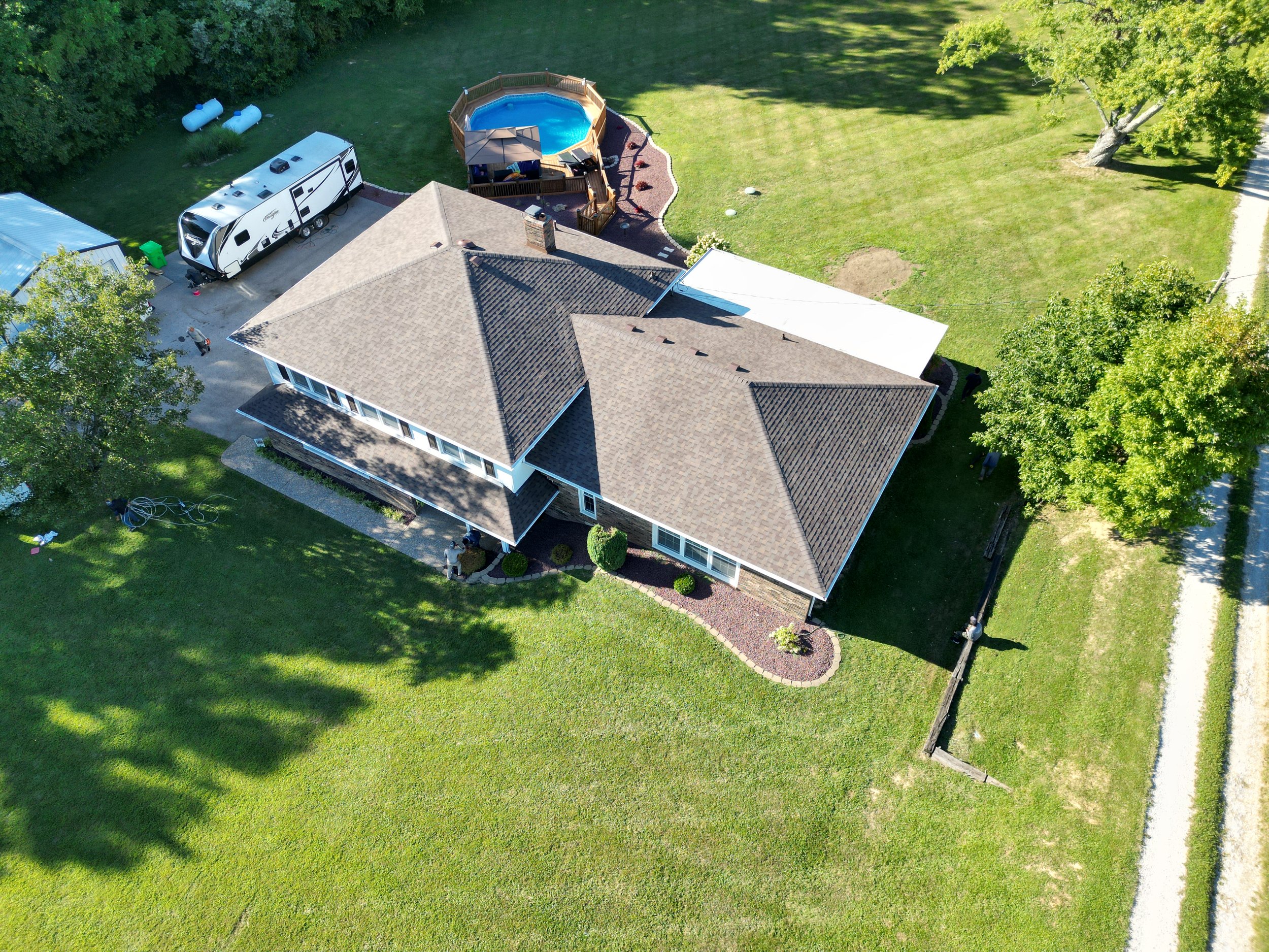 Aerial view of a house with a large yard, pool, and camper, surrounded by trees and grass.