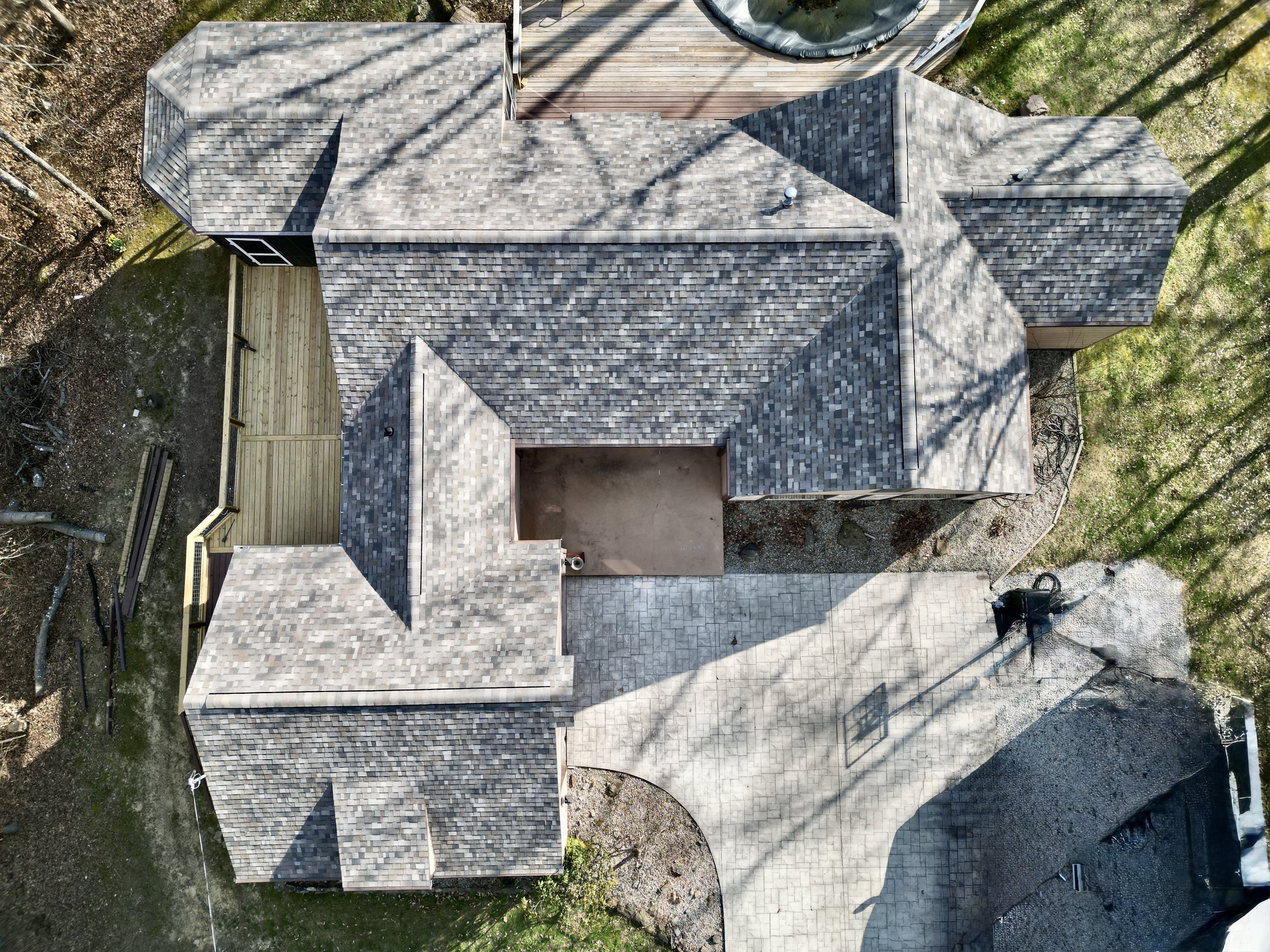 Aerial view of a house with multiple roof sections, a newly built wooden deck, a concrete patio, and surrounding trees.