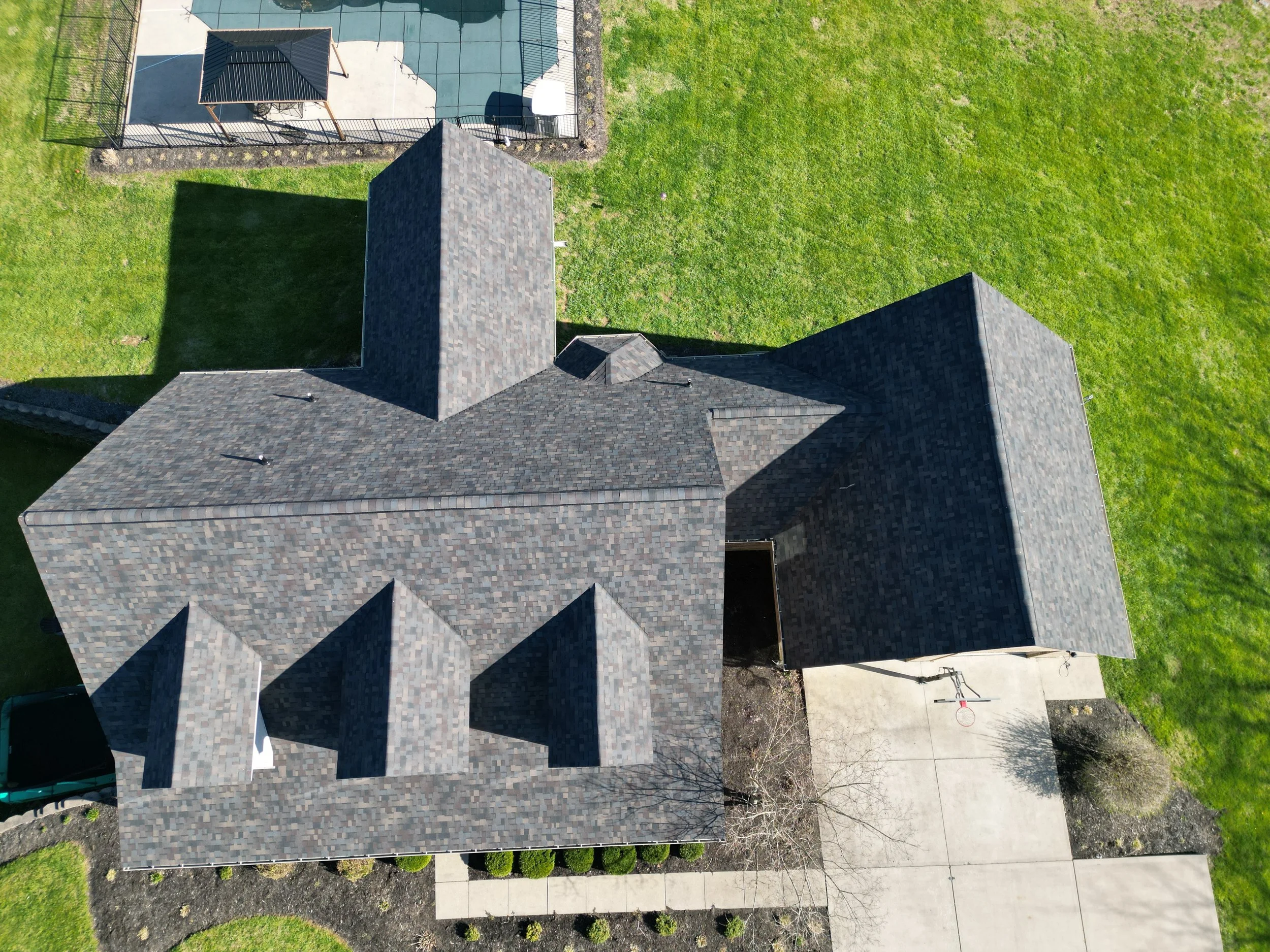Aerial view of a house with a dark shingle roof and a backyard with a sports court.