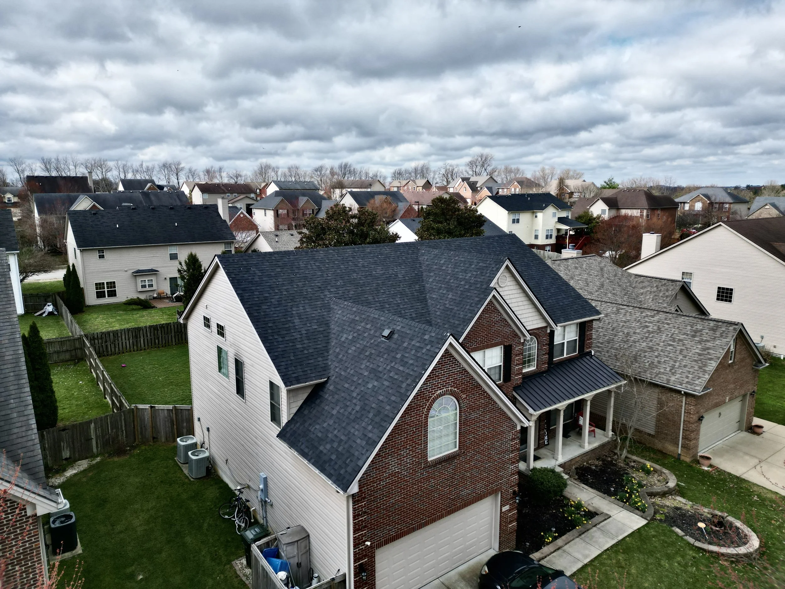 An aerial view of a suburban neighborhood with houses, fences, and trees under a cloudy sky.
