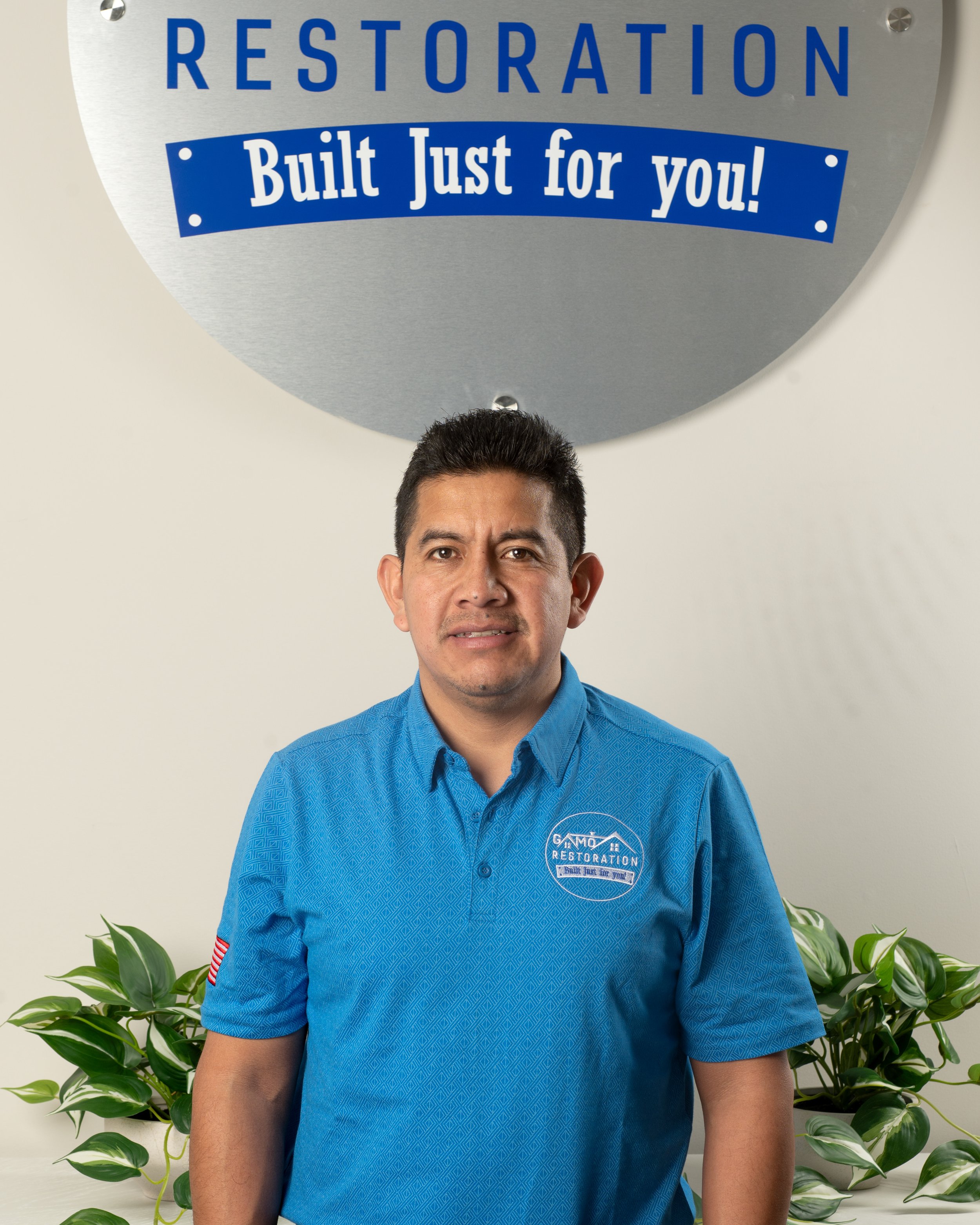 Man in blue shirt standing in front of a sign reading 'Restoration Built Just for You!'