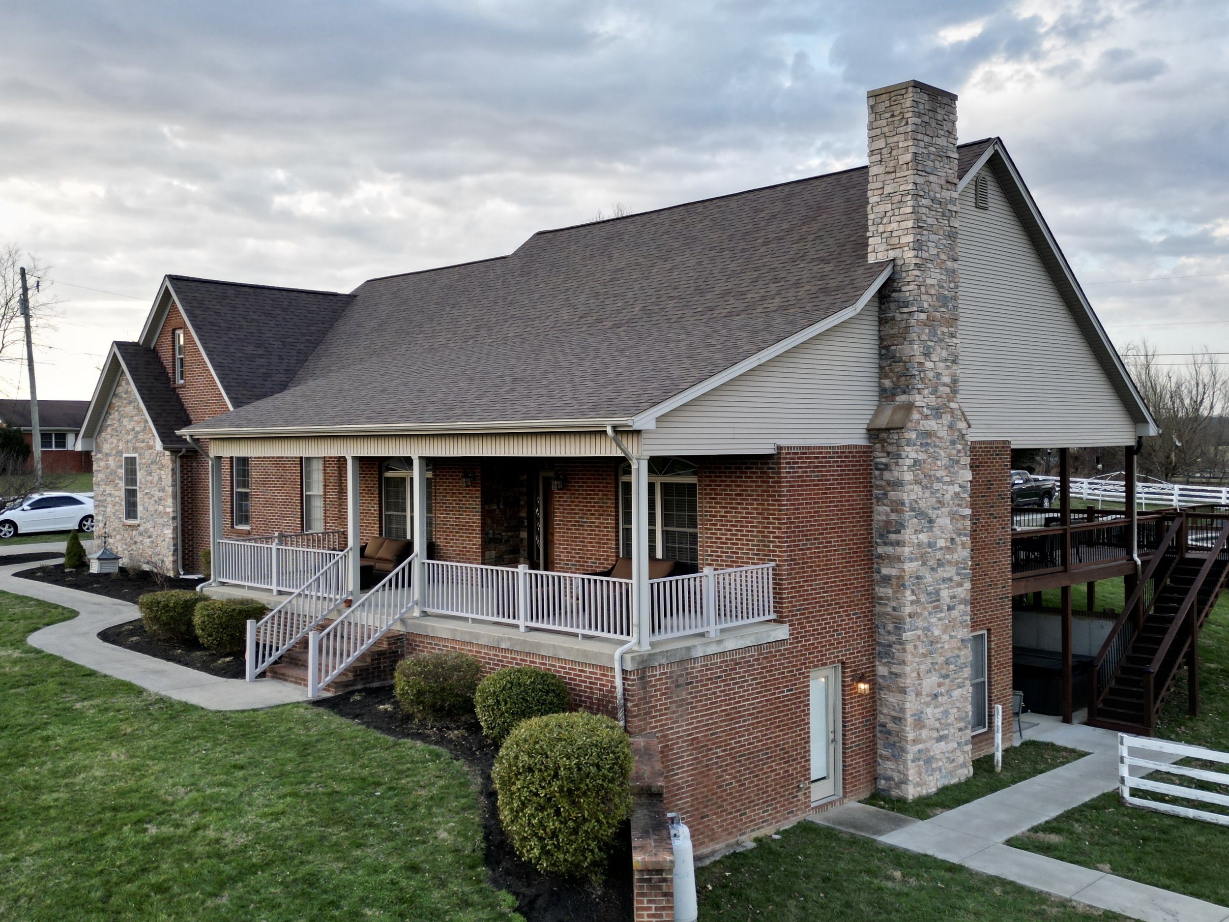 A two-story suburban house with brick and stone exterior, a large chimney, front porch, stairs, and well-maintained lawn.