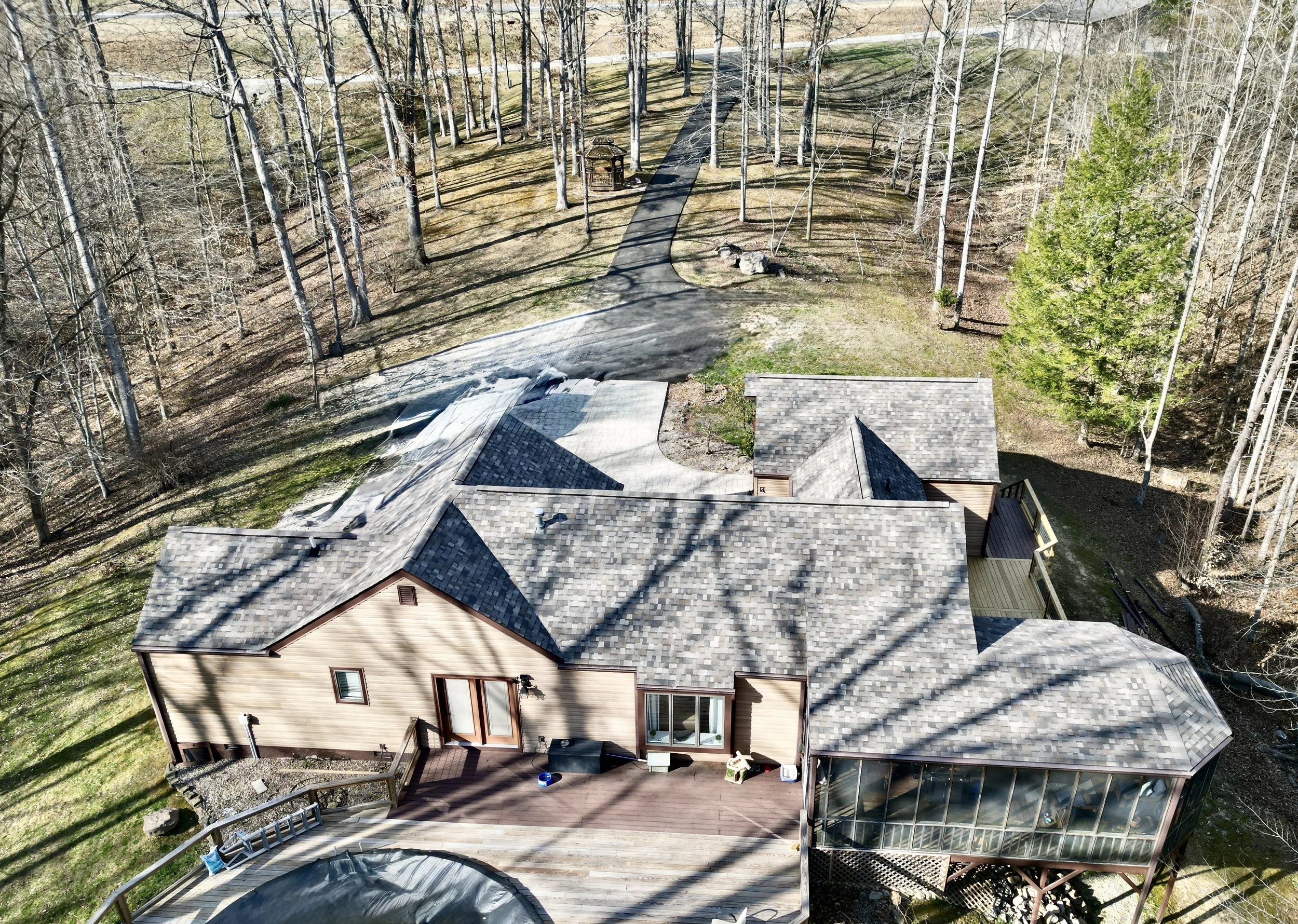 Aerial view of a house with a large deck, surrounded by trees and a winding driveway in a wooded area.