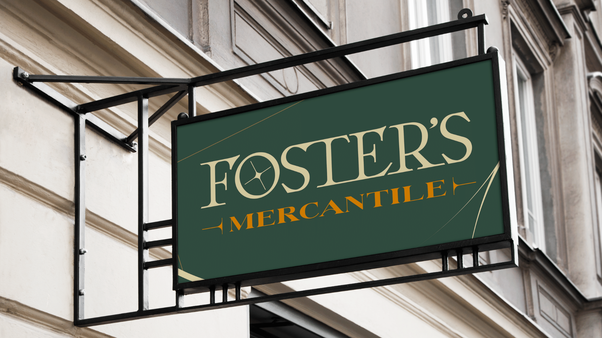A green rectangular sign with the text "FOSTER'S MERCANTILE" in beige and orange, hanging on the exterior wall of a building with decorative molding.
