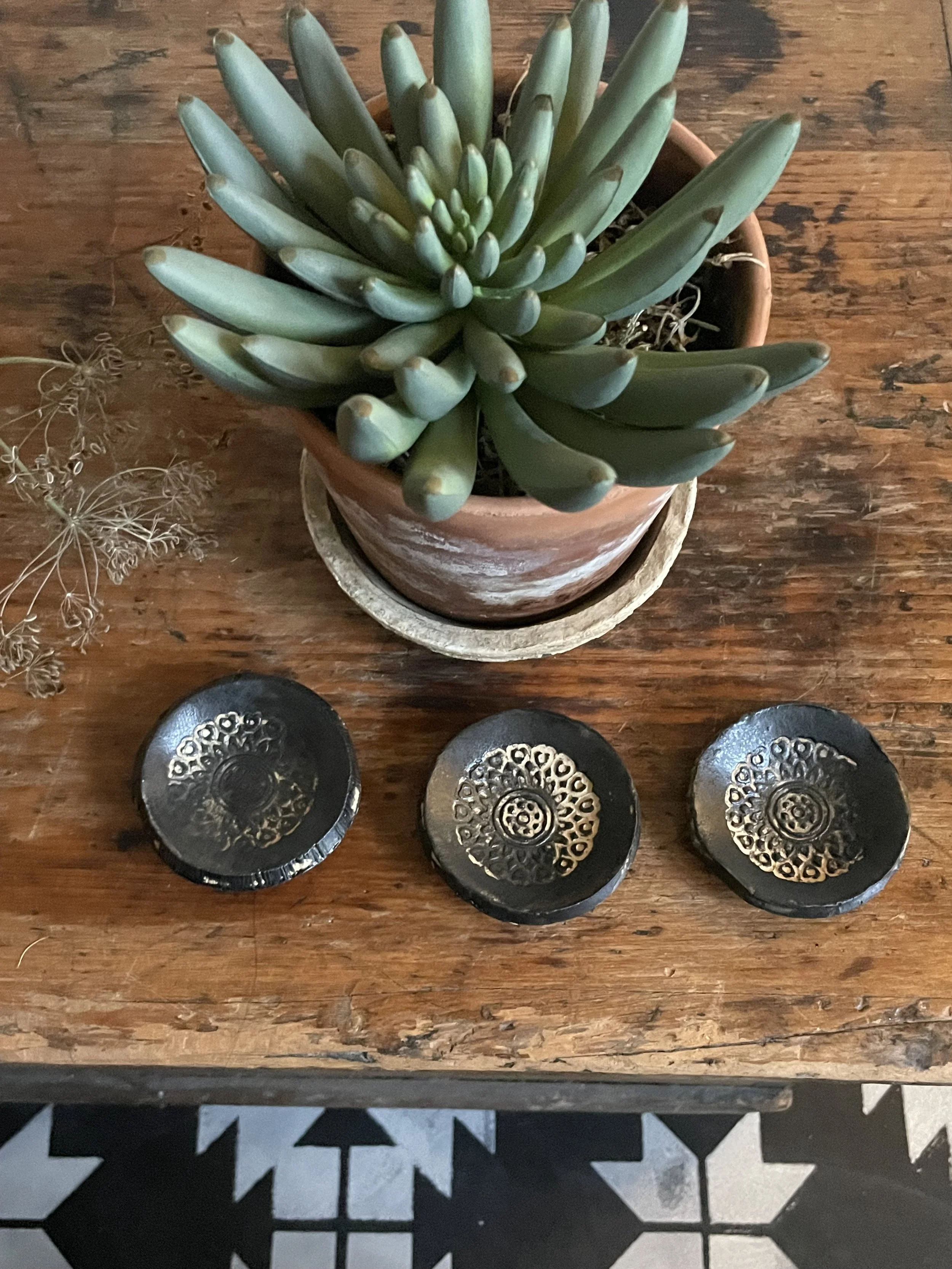 Top view of a potted succulent plant on a wooden surface with three decorative black stones with gold geometric patterns in front of it.