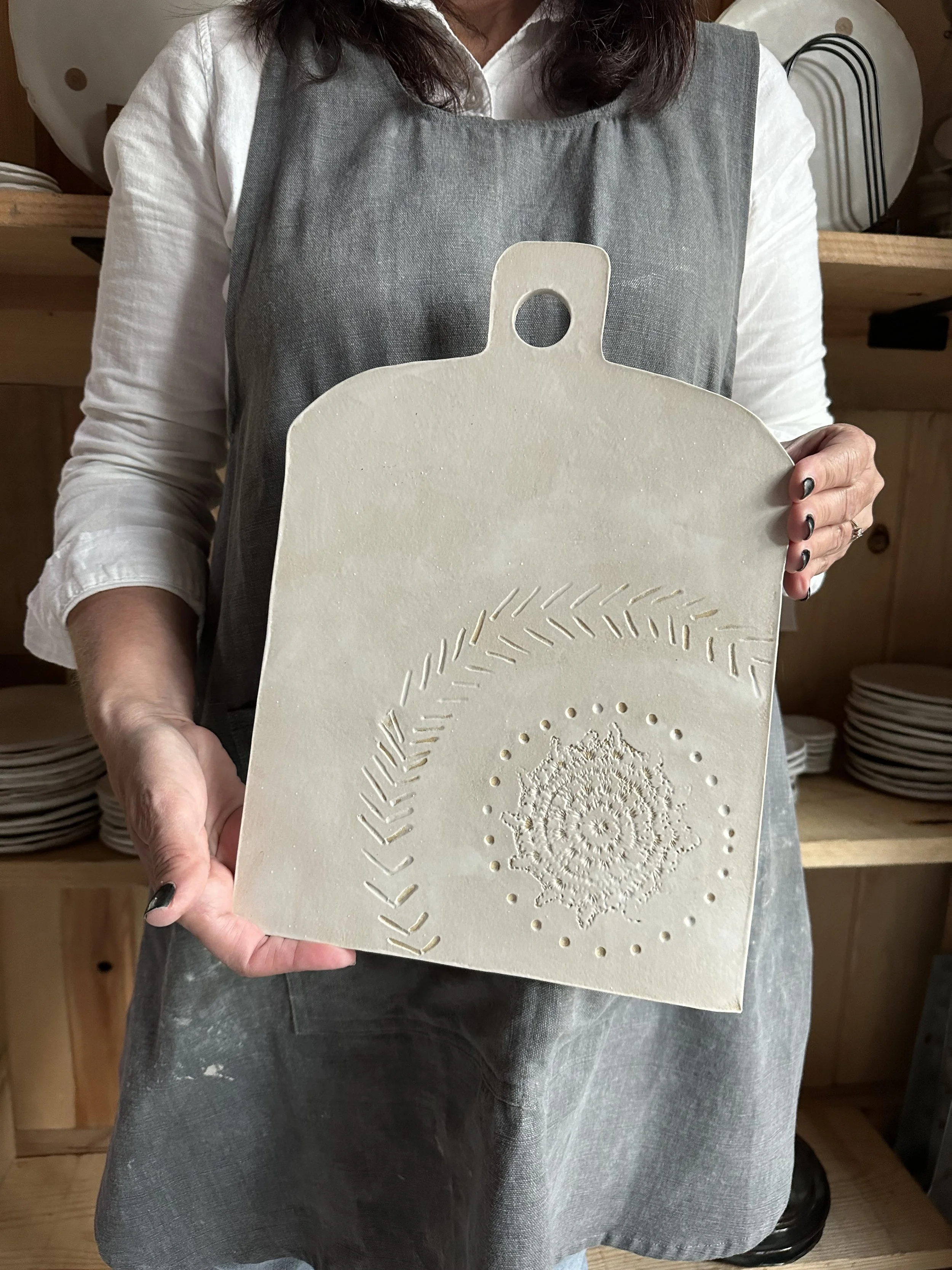 Woman in a grey apron holding a rectangular mold with embossed decorative patterns.