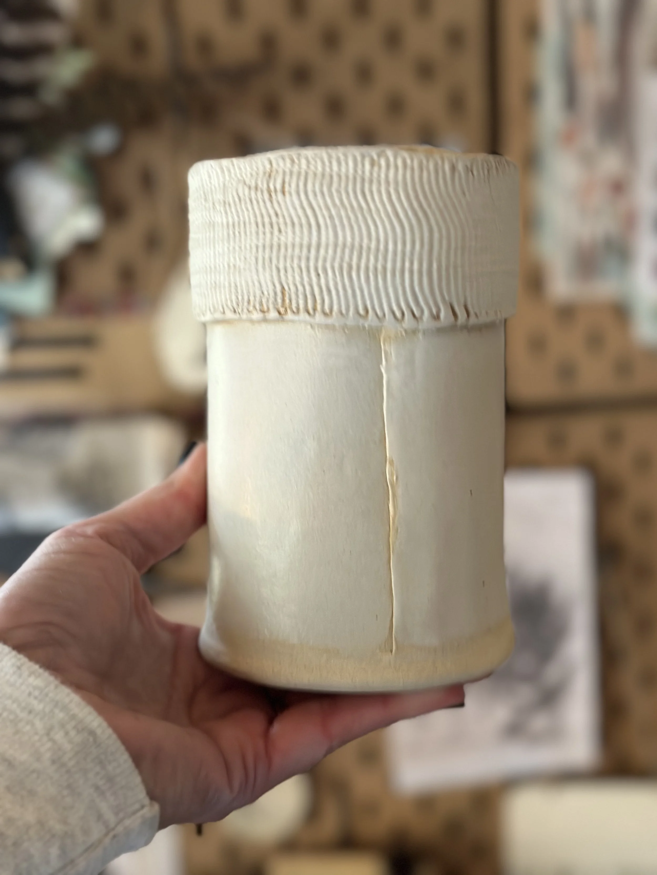 A hand holding a cylindrical container with a textured lid in an indoor setting.