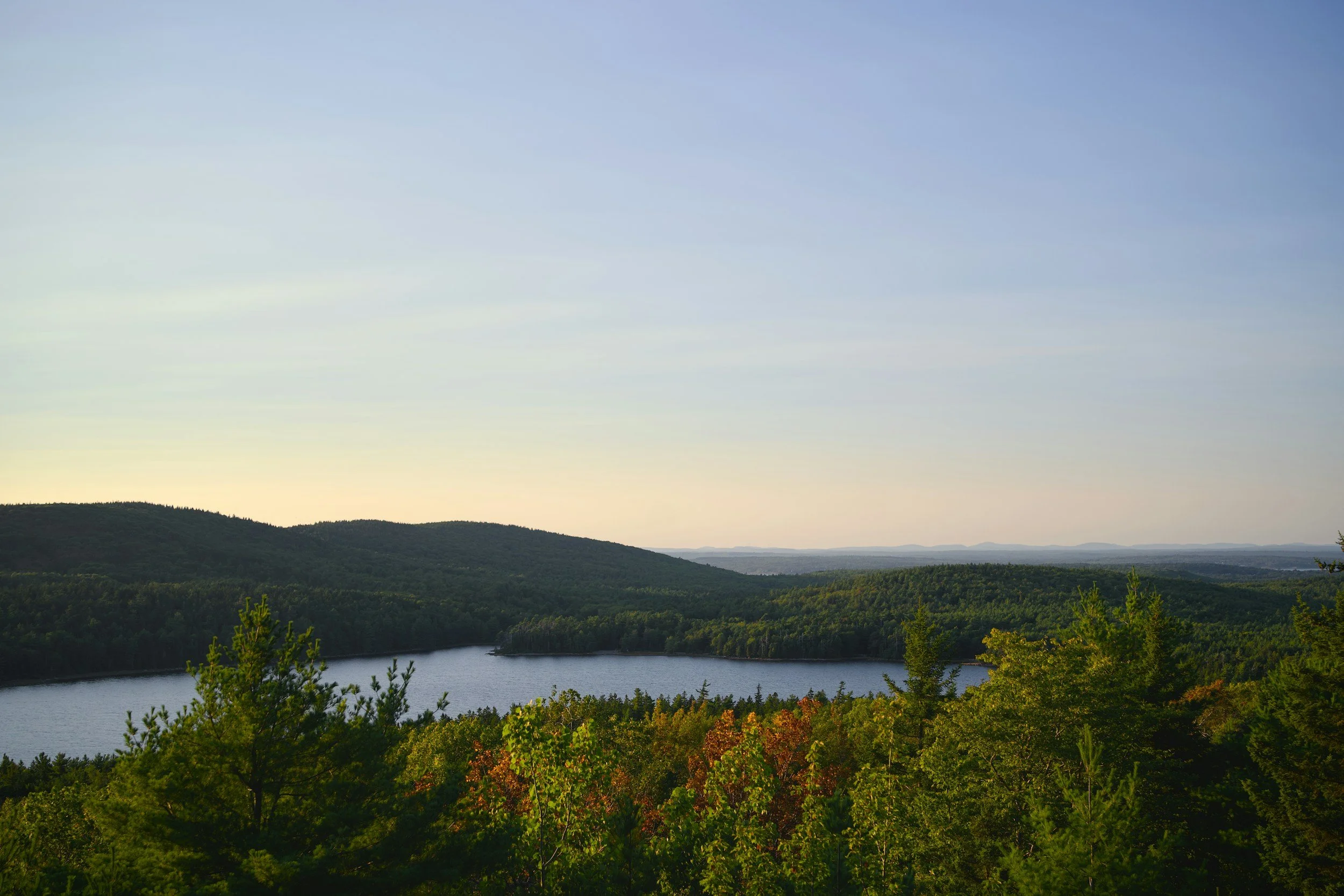 Sunrise over a calm lake surrounded by wooded hills