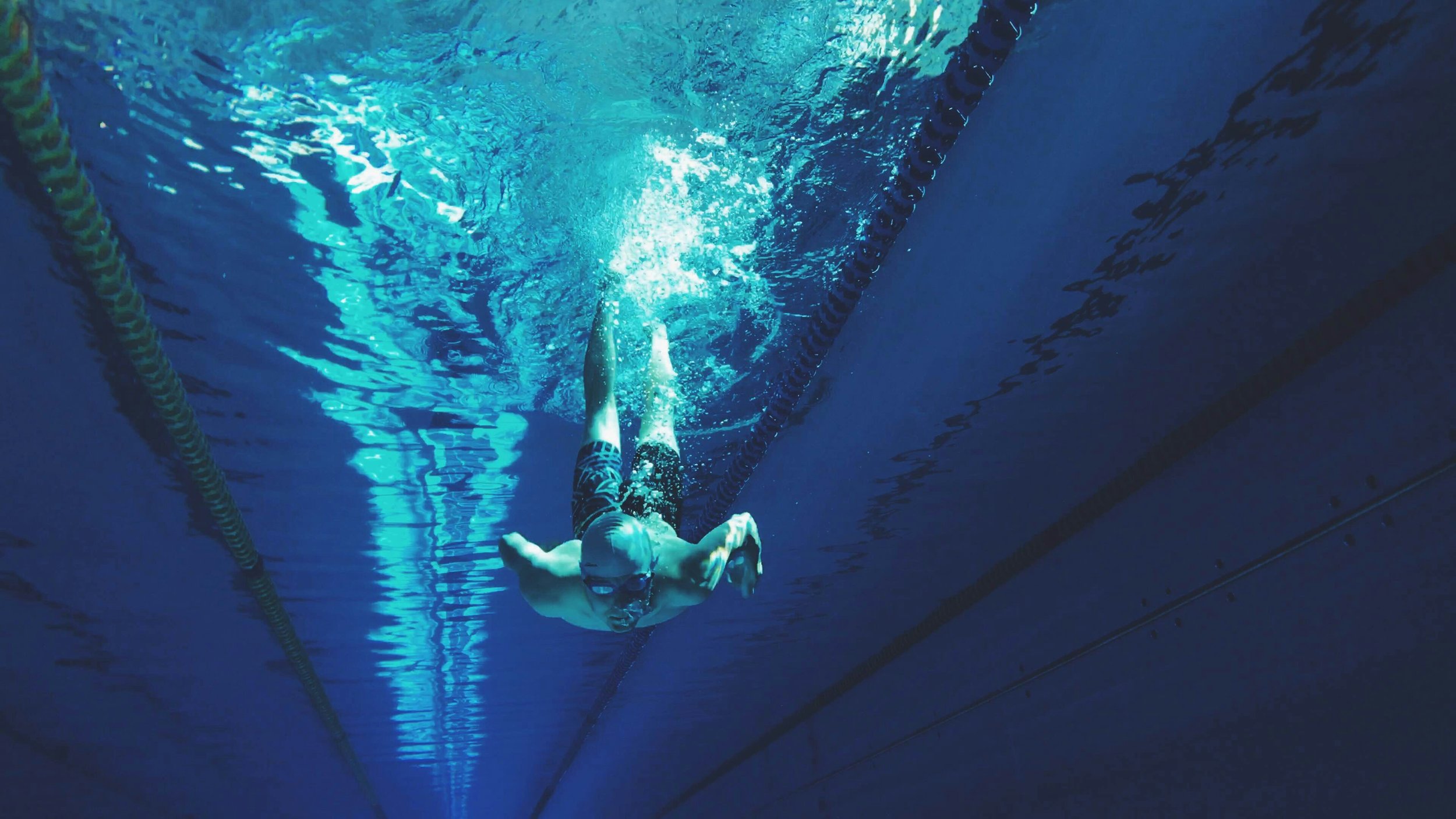 An underwater view of a swimmer wearing goggles, swimming in a pool with lane markers.