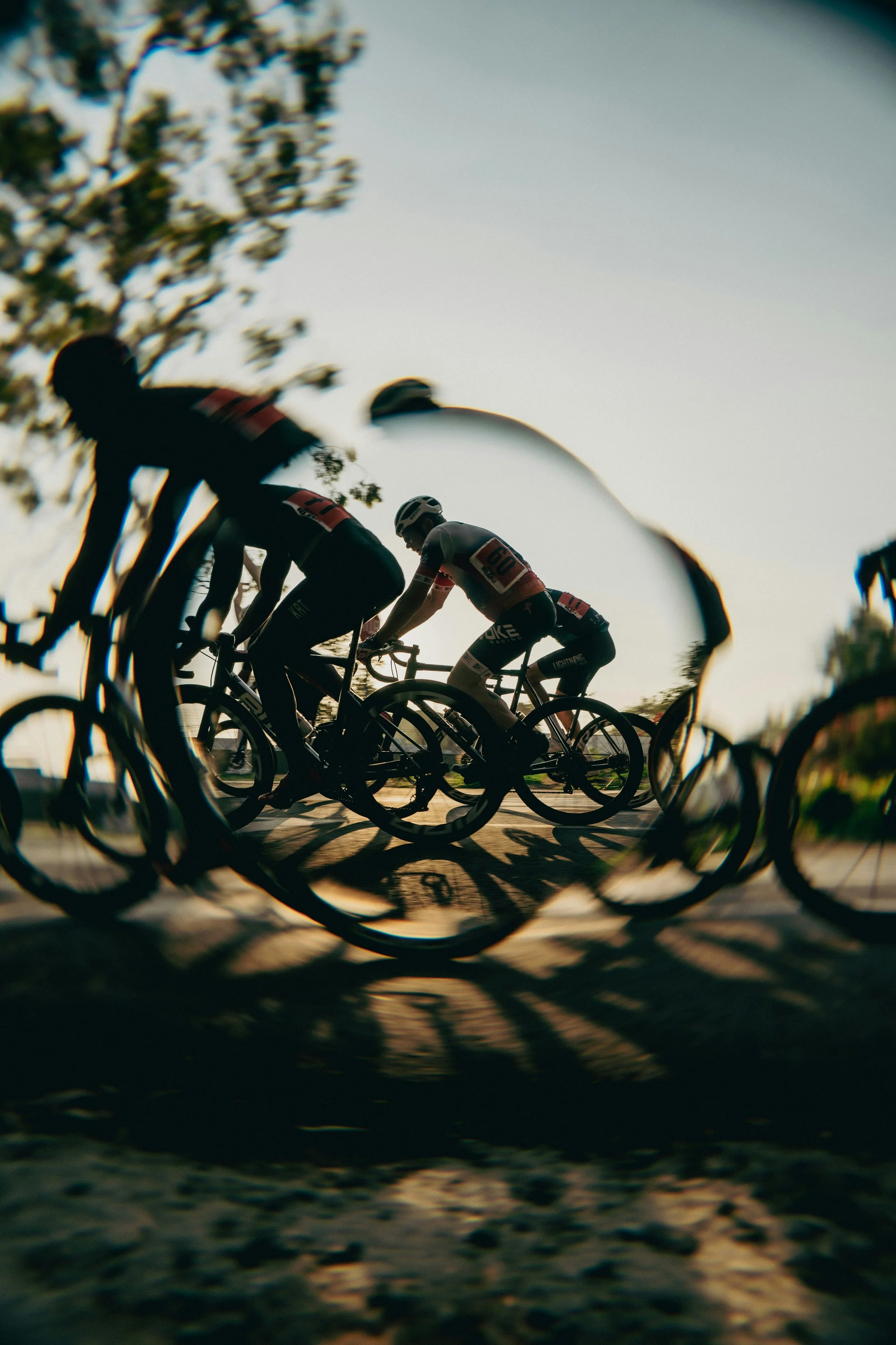 Cyclists riding bicycles during sunset, viewed through a heart-shaped object.