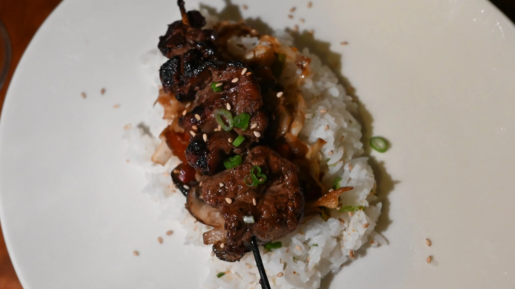 Grilled flank steak skewers with chopped green onions and sesame seeds served on white rice with vegetables.