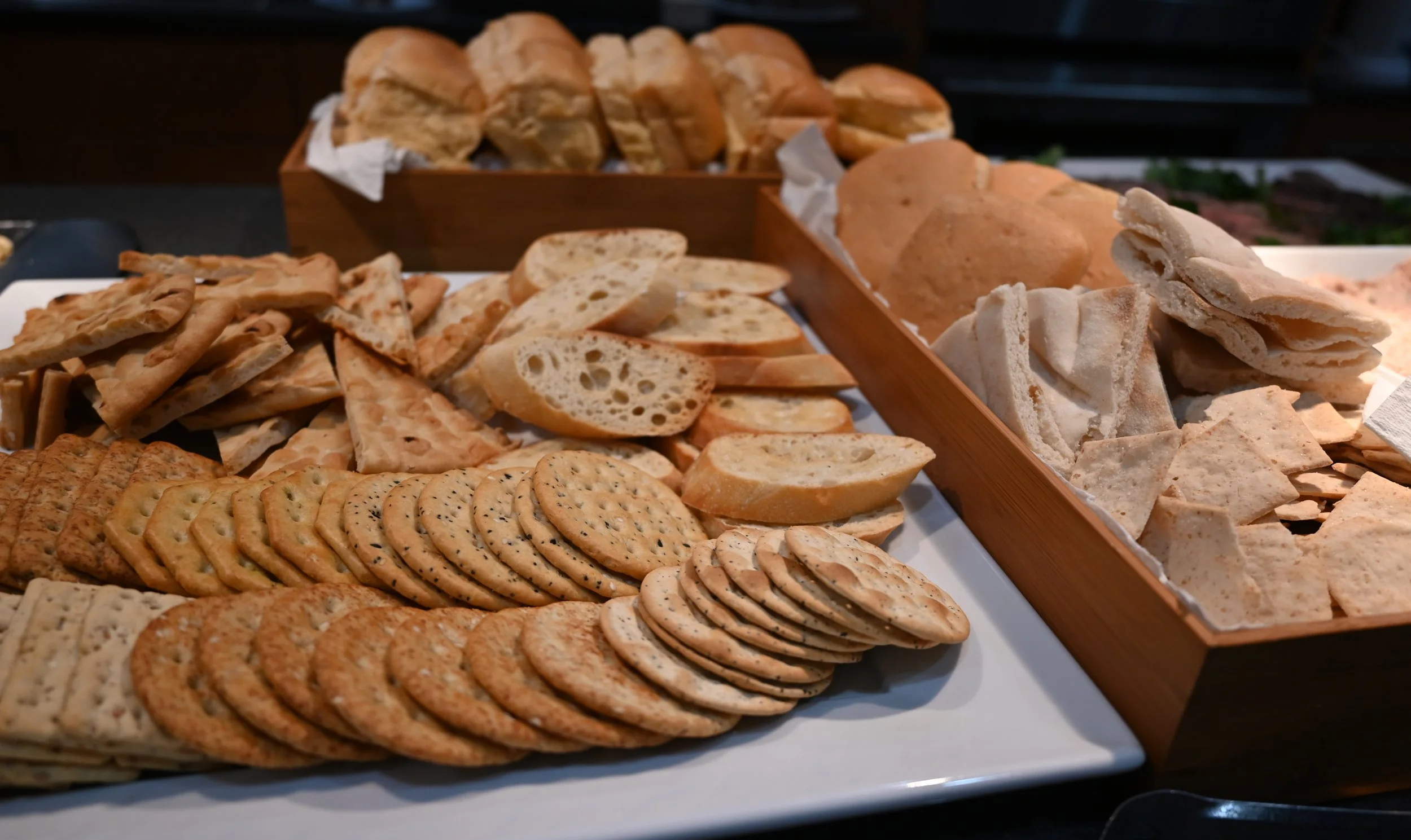 A variety of bread and crackers on a white platter and wooden trays.