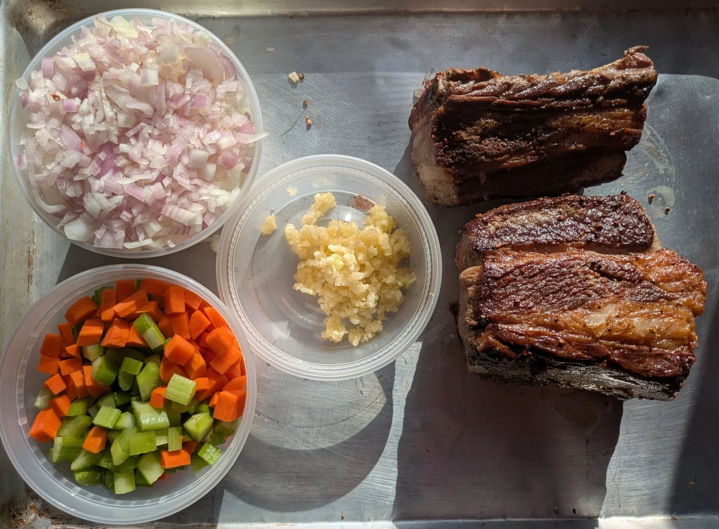 Chopped shallot, minced garlic, diced carrots and celery, seared Ohio local beef ribs on a metal sheet tray.