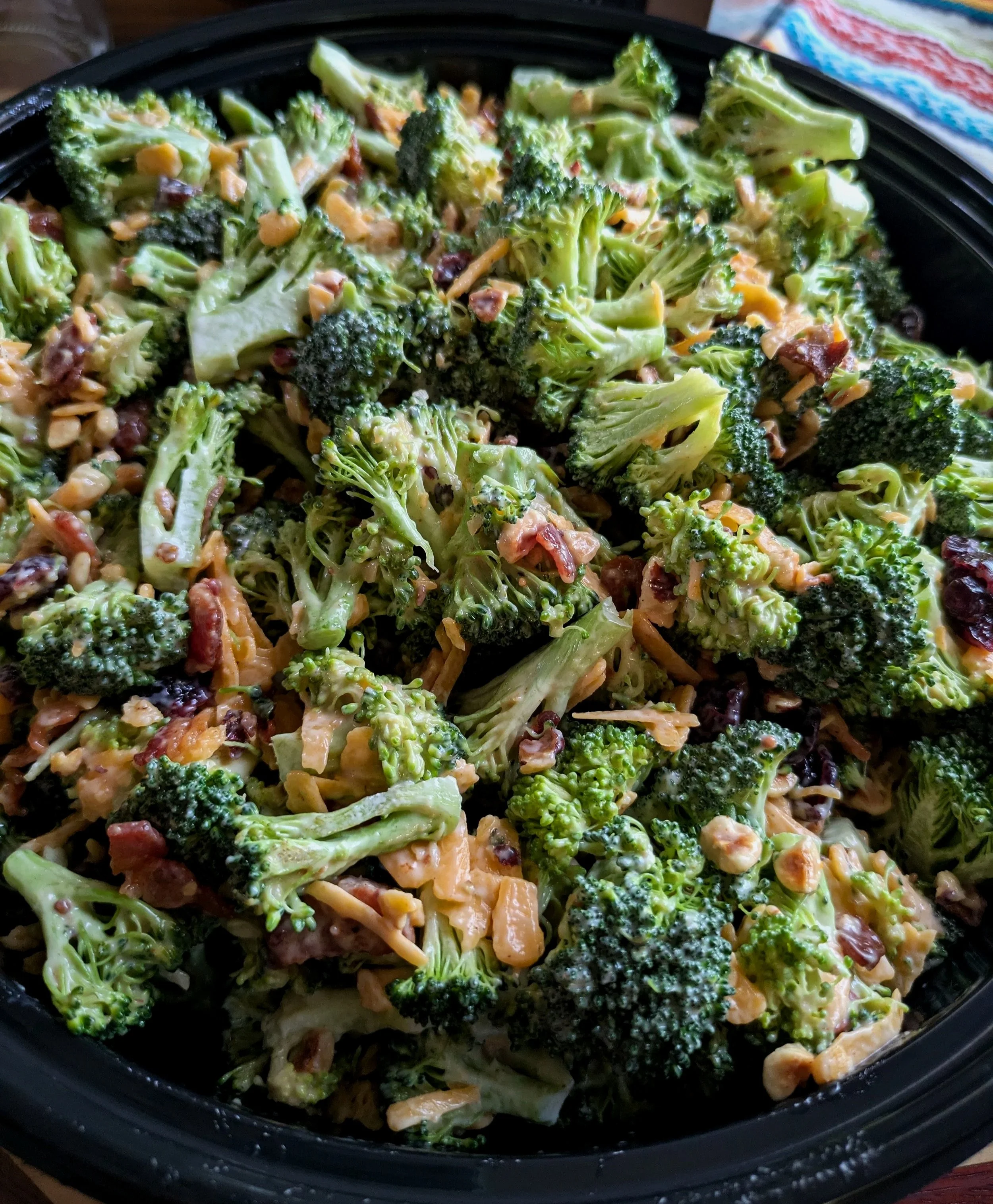 Vegetable salad with broccoli florets, shredded cheese, and chopped nuts in a black bowl.