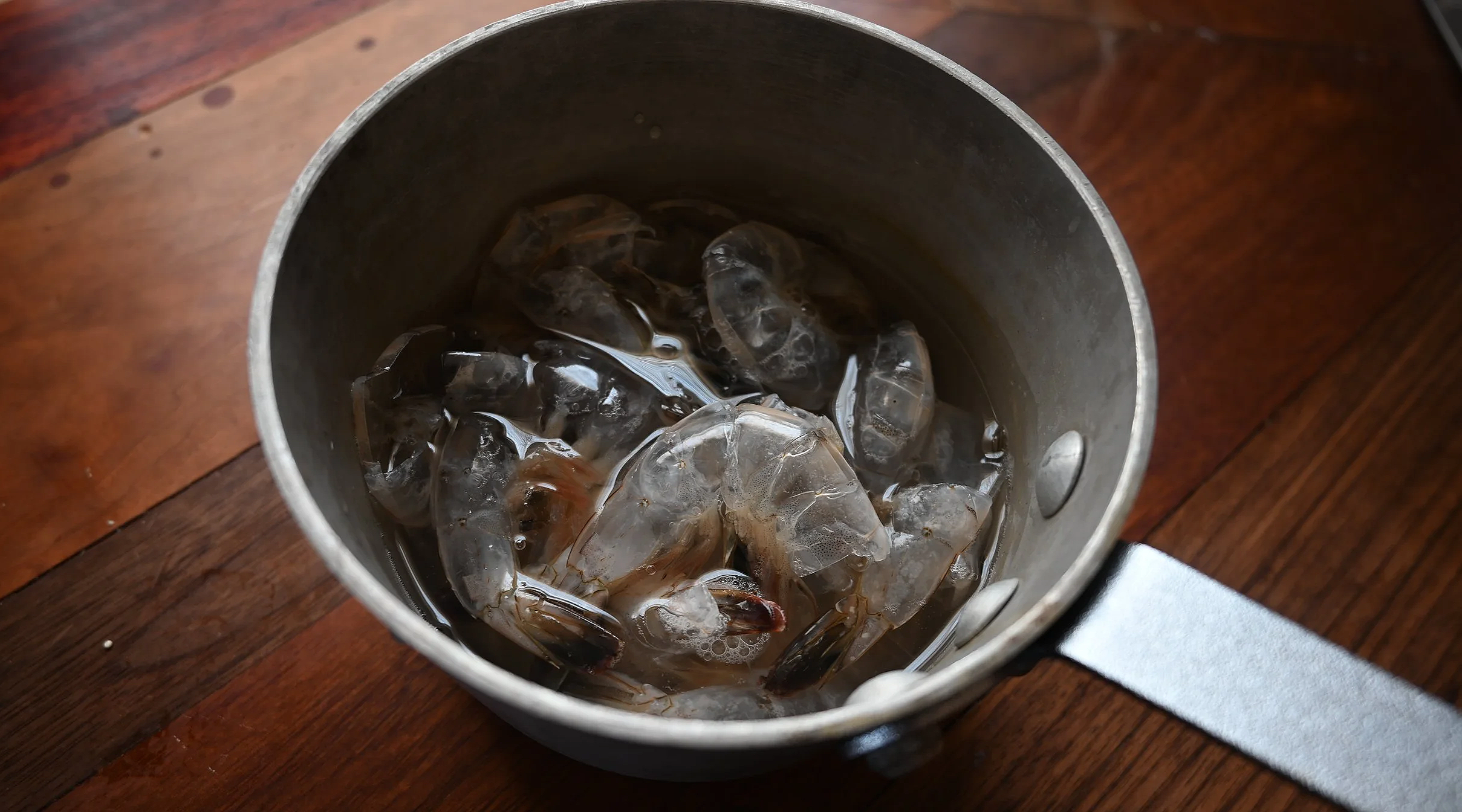 A small pot filled with shrimp shells and water for a stock on a wooden surface.