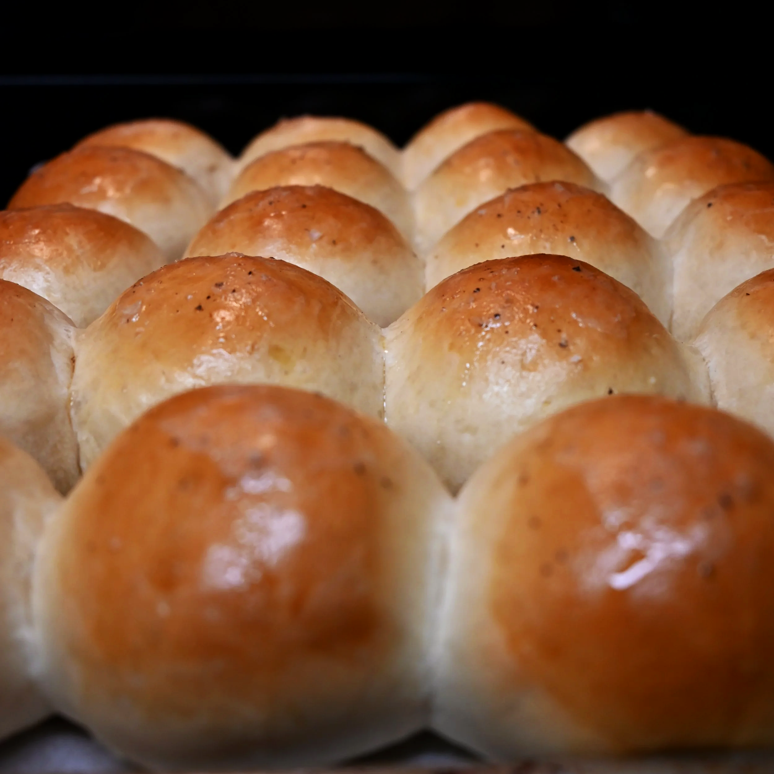 Close-up of golden-brown dinner rolls arranged on a baking sheet.