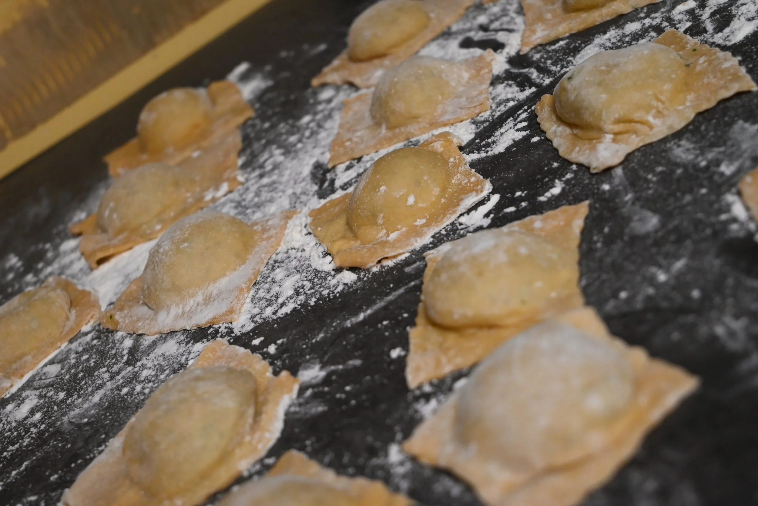 Homemade uncooked ravioli, dusted with flour, on a floured counter.