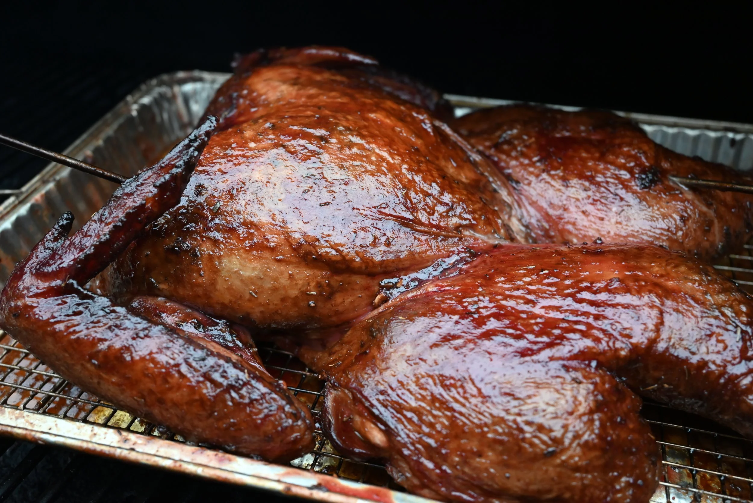 Whole smoked turkey with shiny, glazed skin on a smoker