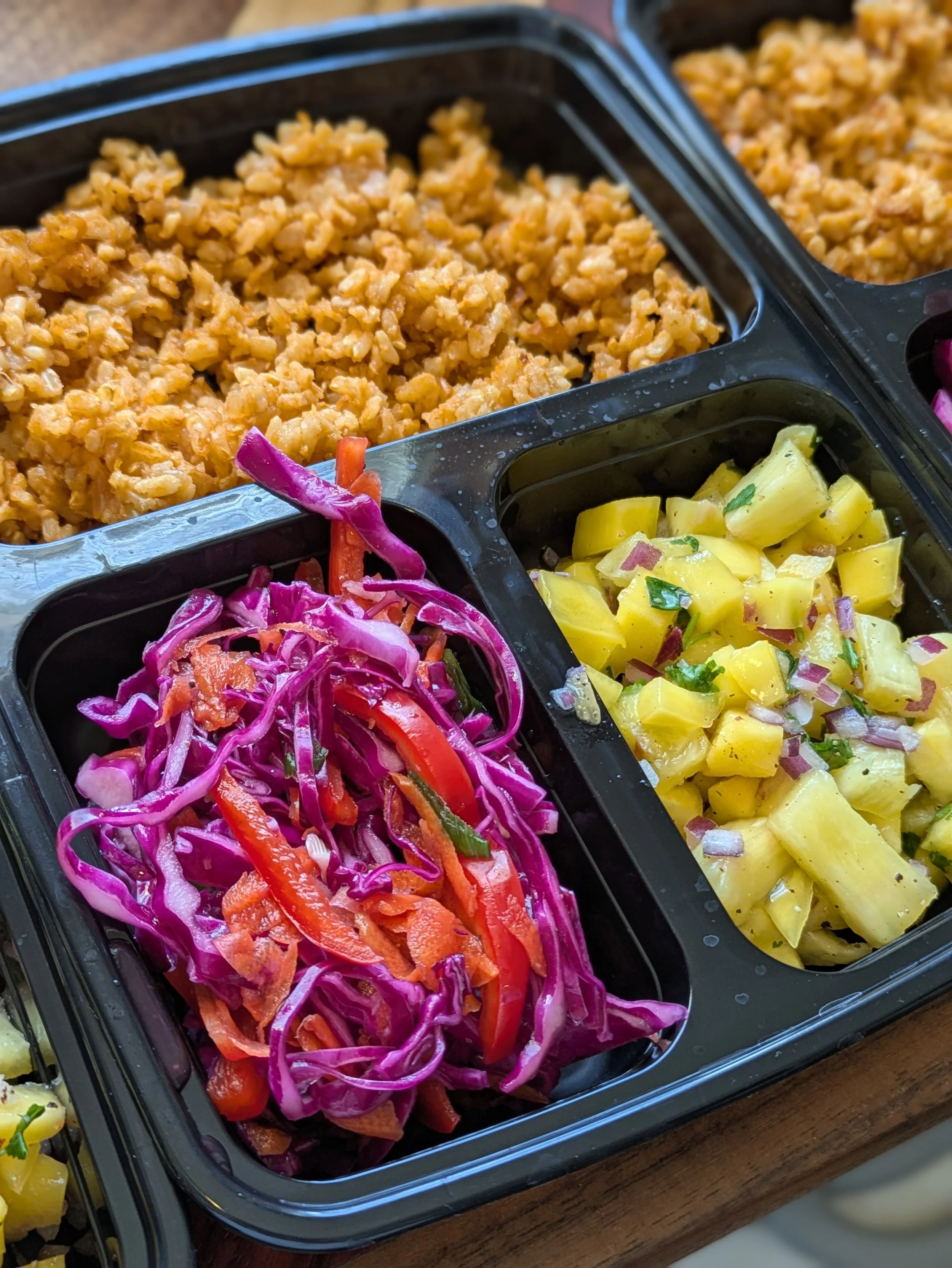 Meal prep containers with seasoned ground meat, diced pineapple salad with herbs, and purple cabbage slaw with carrots and bell peppers.