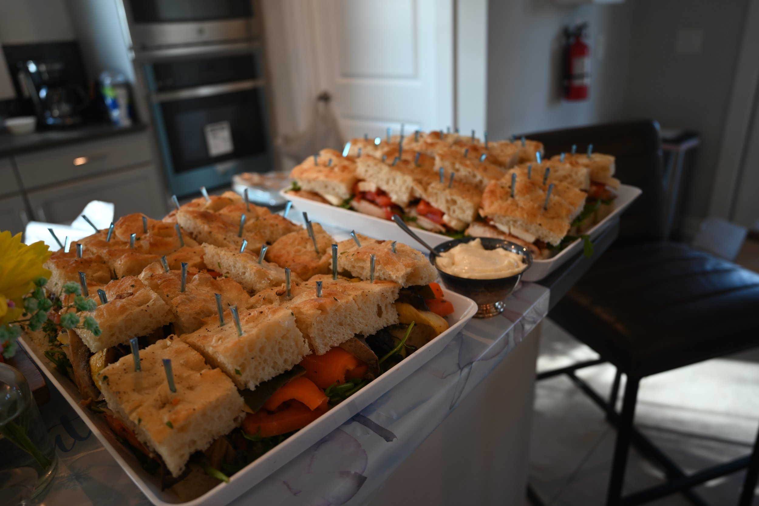 Platter of cut sandwiches with toothpick picks, next to a bowl of dip, on a table in a kitchen.