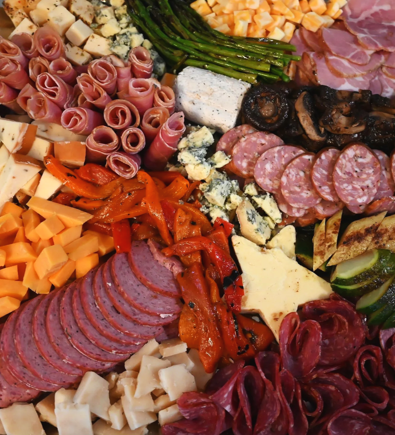 Assorted charcuterie board with cheeses, cured meats, roasted peppers, and vegetables.