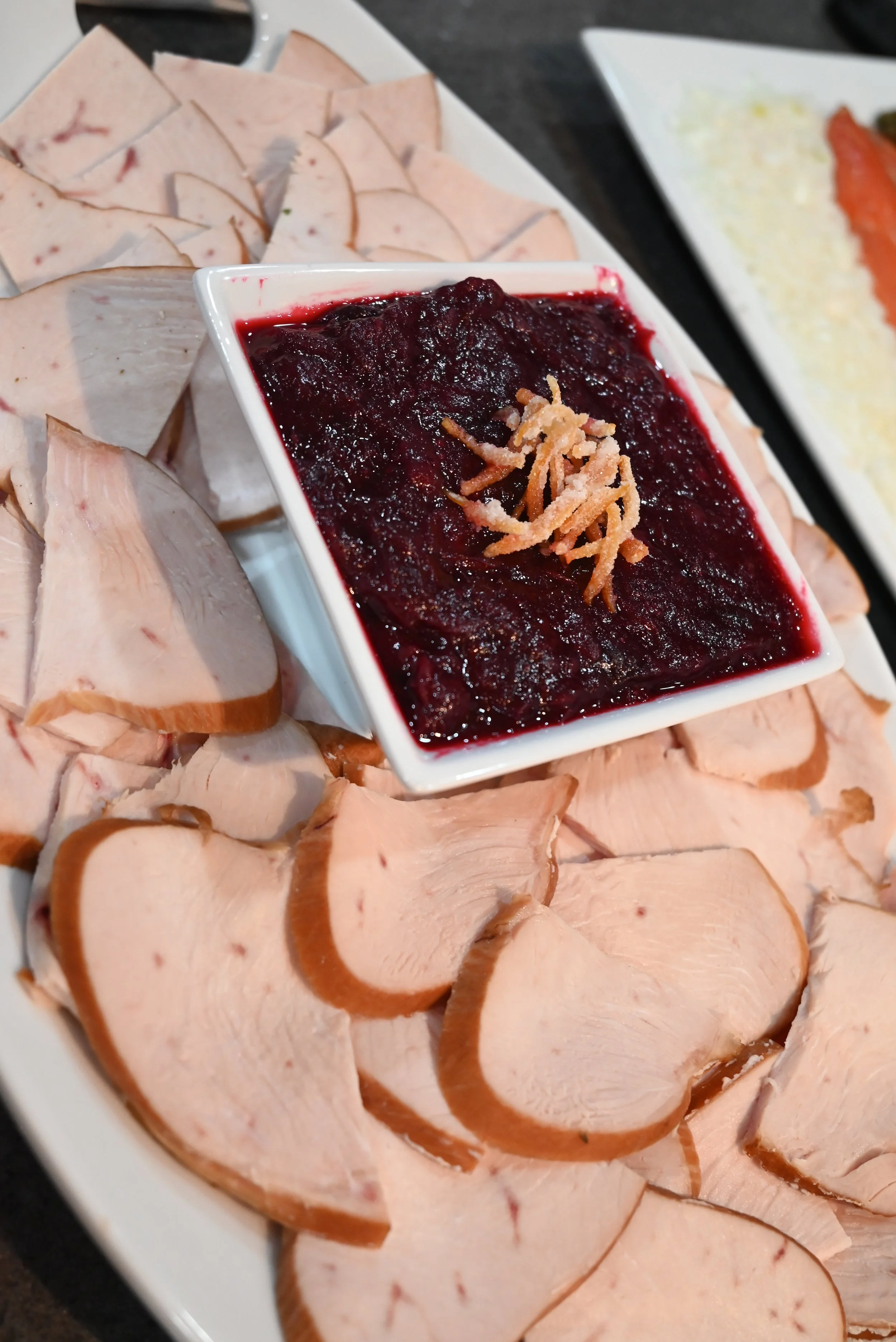 Slices of smoked turkey breast arranged on a white platter with a small dish of cranberry sauce in the center.